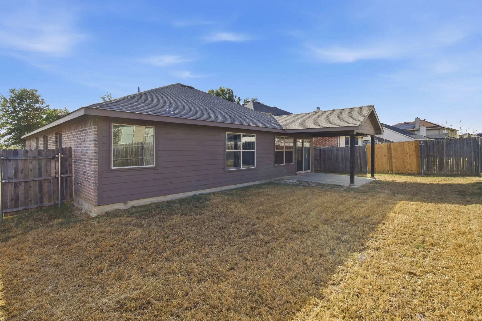 Expansive backyard featuring a covered patio, wood fencing, and brick exterior accents