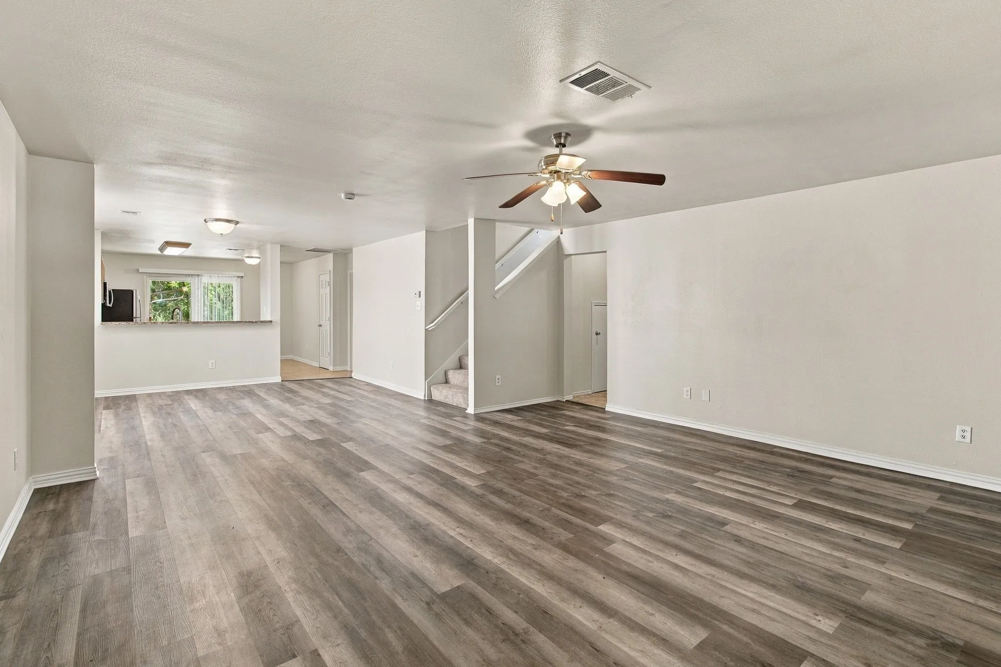Expansive open concept living area featuring wood-finish flooring, a ceiling fan with integrated lighting, and neutral wall tones