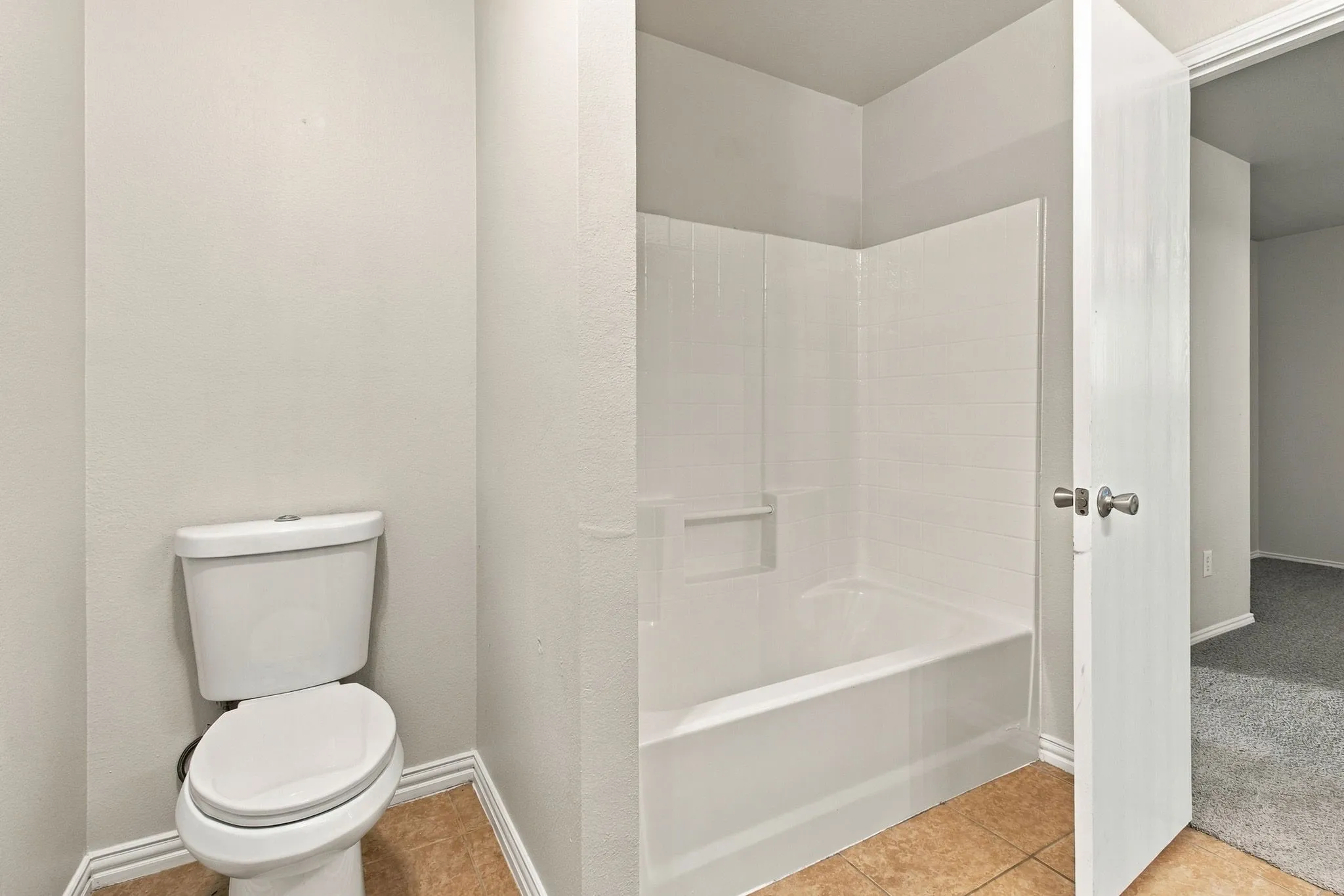 Bathroom with a white toilet, white tub and shower surround, and tile flooring