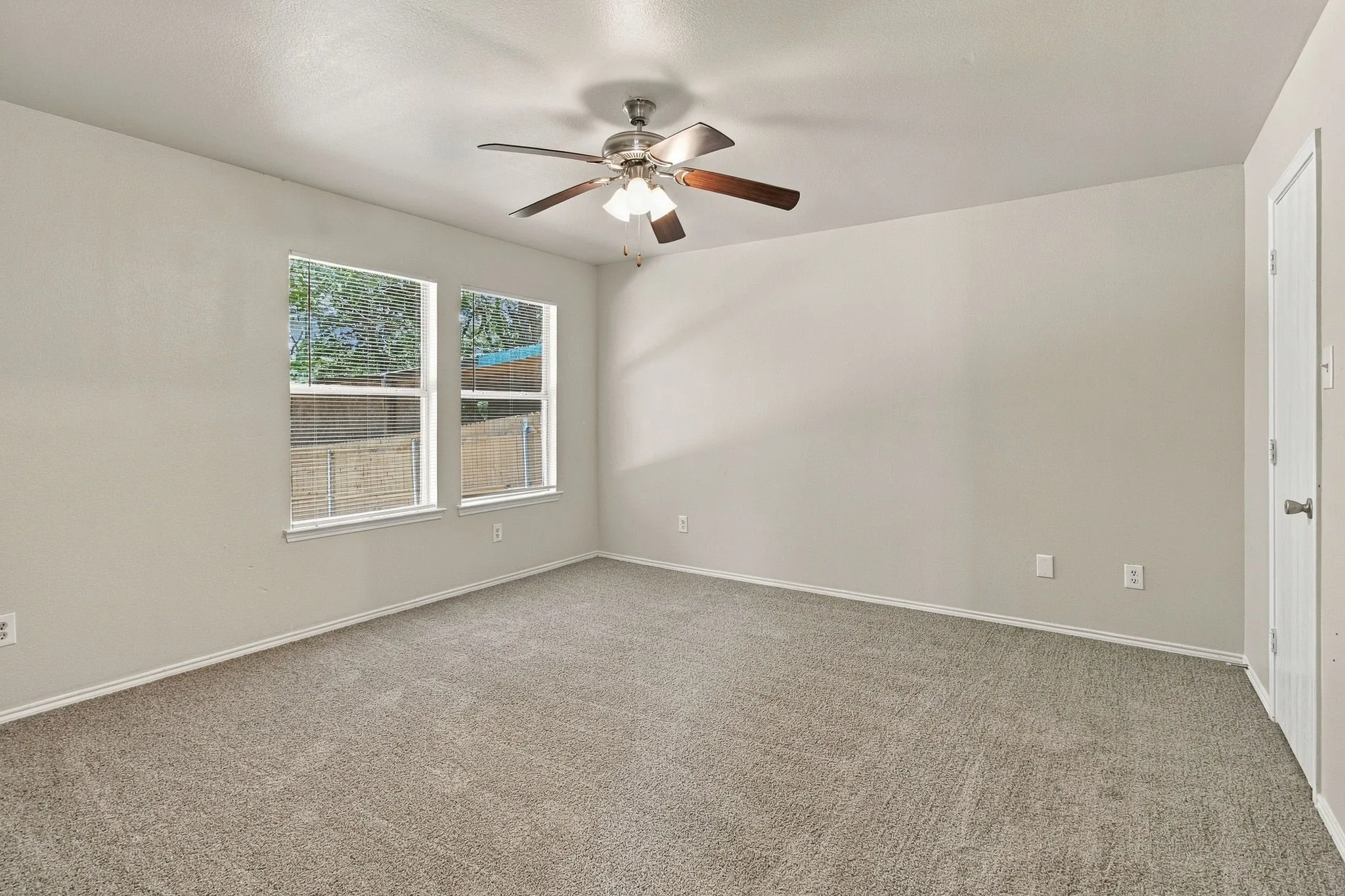 Carpeted room with neutral wall tones, two large windows, a ceiling fan with integrated lighting, and a white interior door