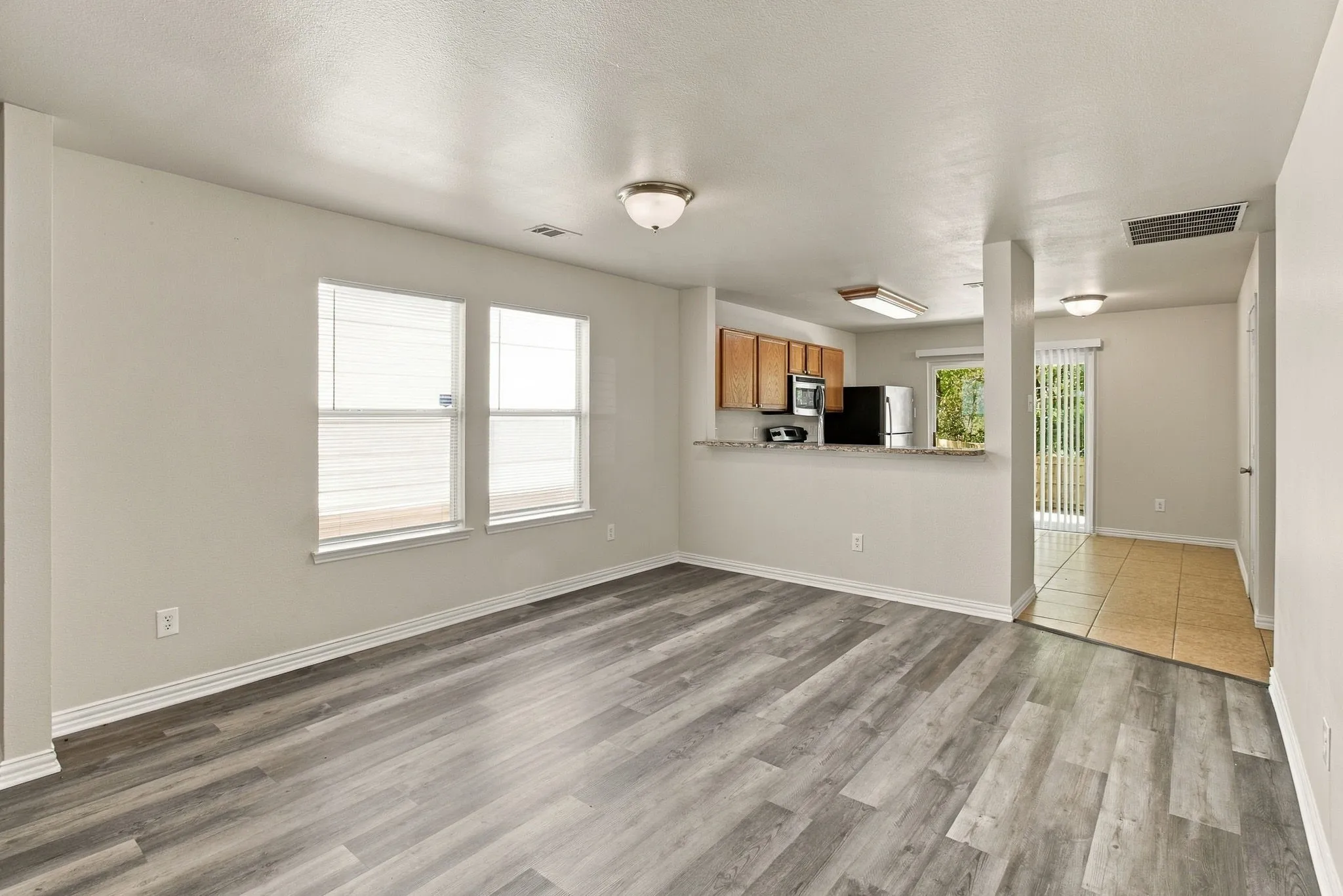 Wood-finish flooring throughout, bright interior with multiple windows, kitchen with wood cabinetry and countertop space, and tiled entry