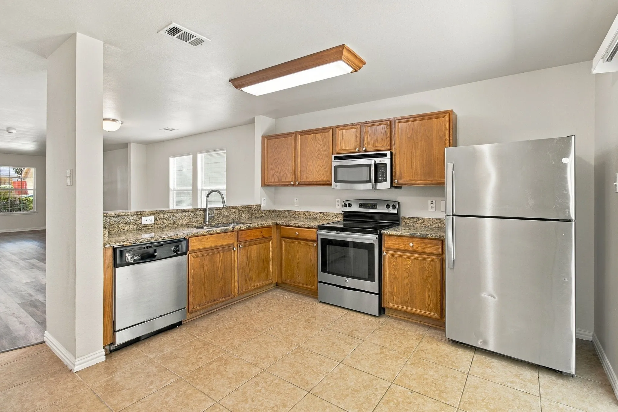 Kitchen featuring stainless steel appliances, wood cabinetry, stone countertops, and tile flooring