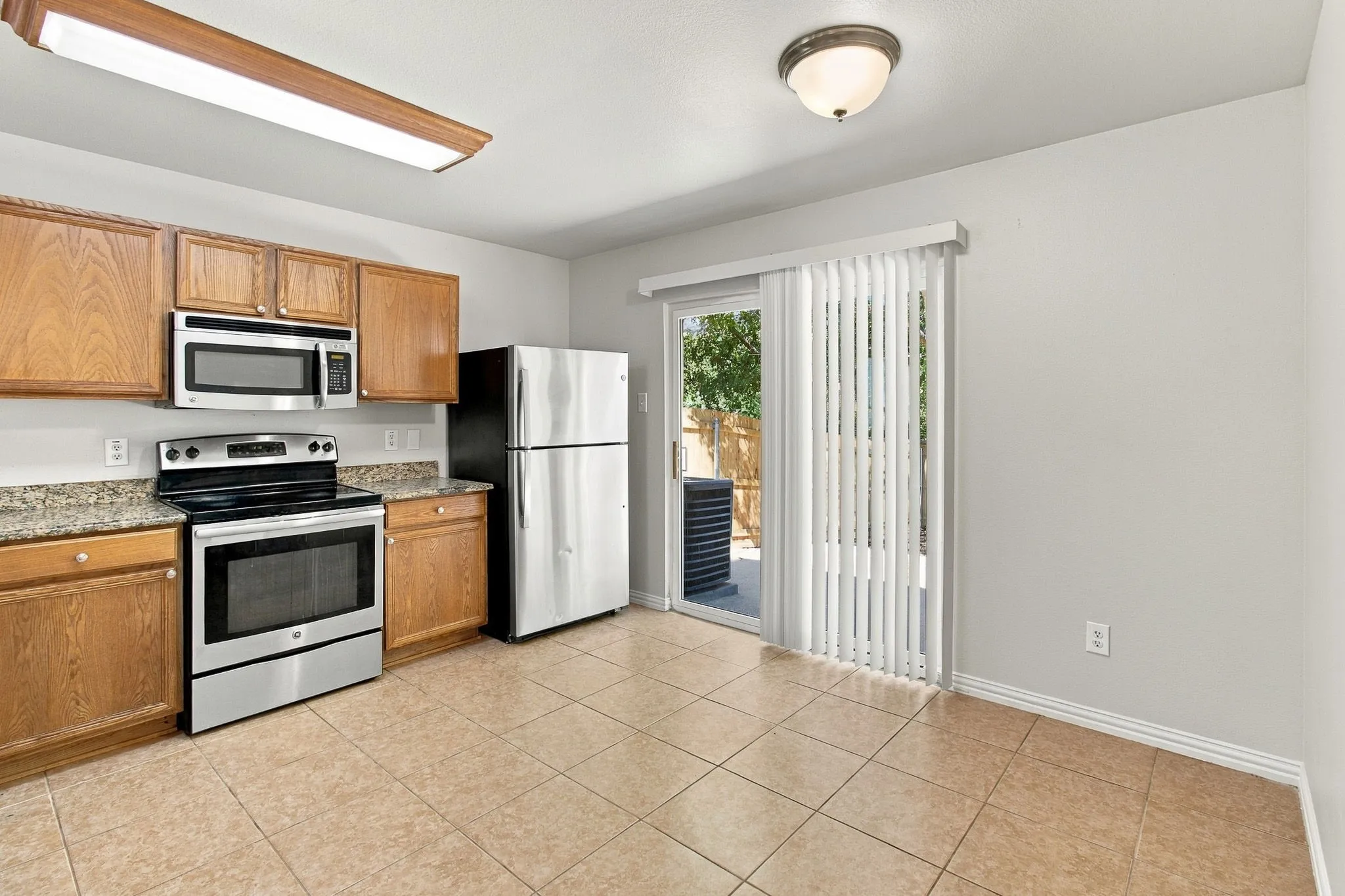 Kitchen featuring wood cabinetry, stainless steel appliances, speckled countertops, and tile flooring