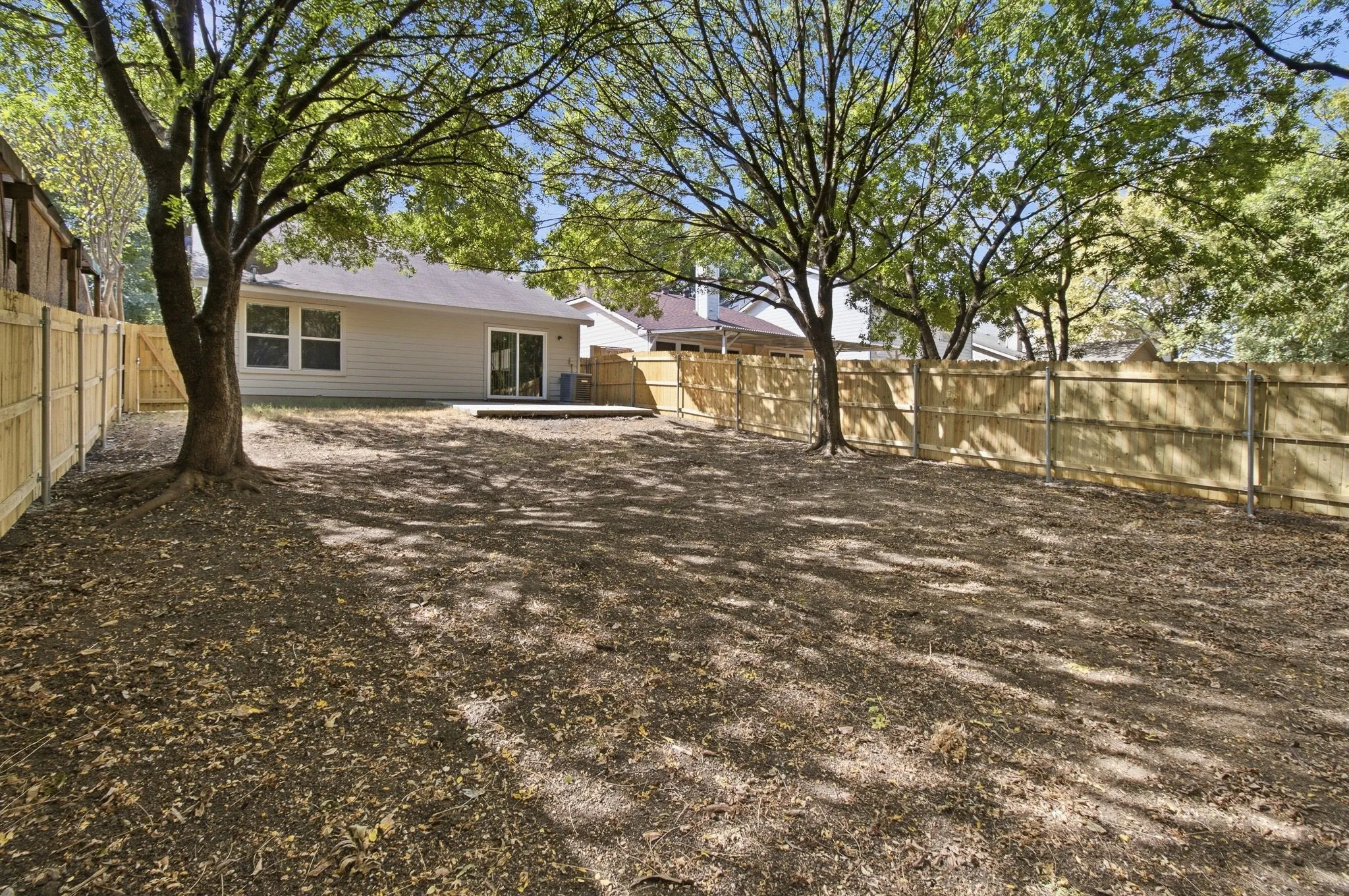 Expansive backyard featuring a complete privacy fence, mature trees, and an exterior deck