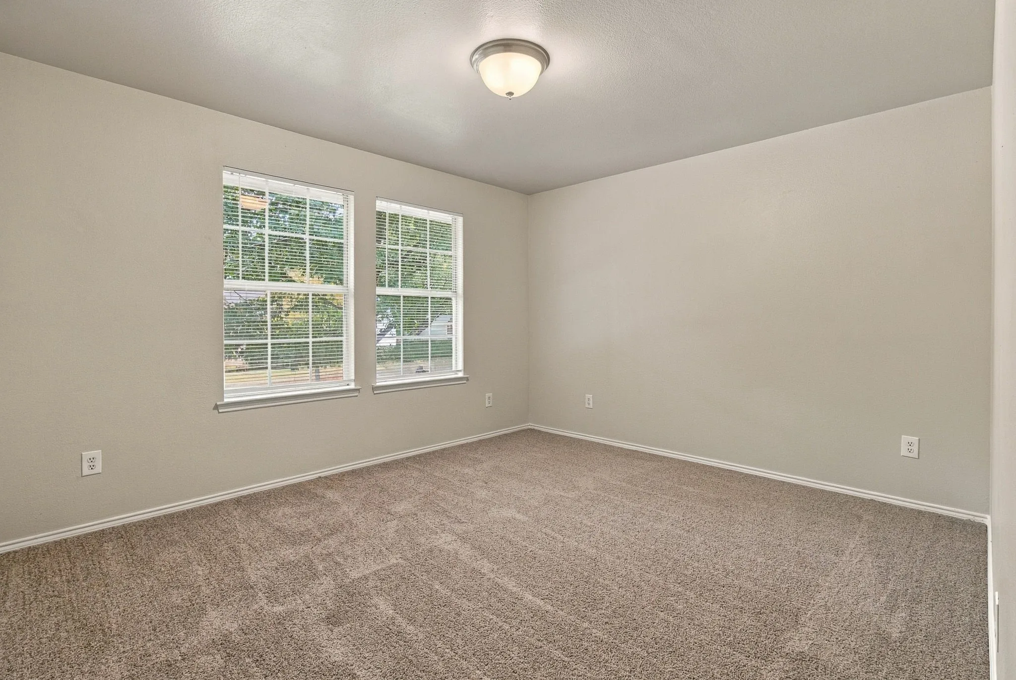 Neutral wall color, two windows with blinds, wall-to-wall carpeting, and a flush-mount ceiling light fixture