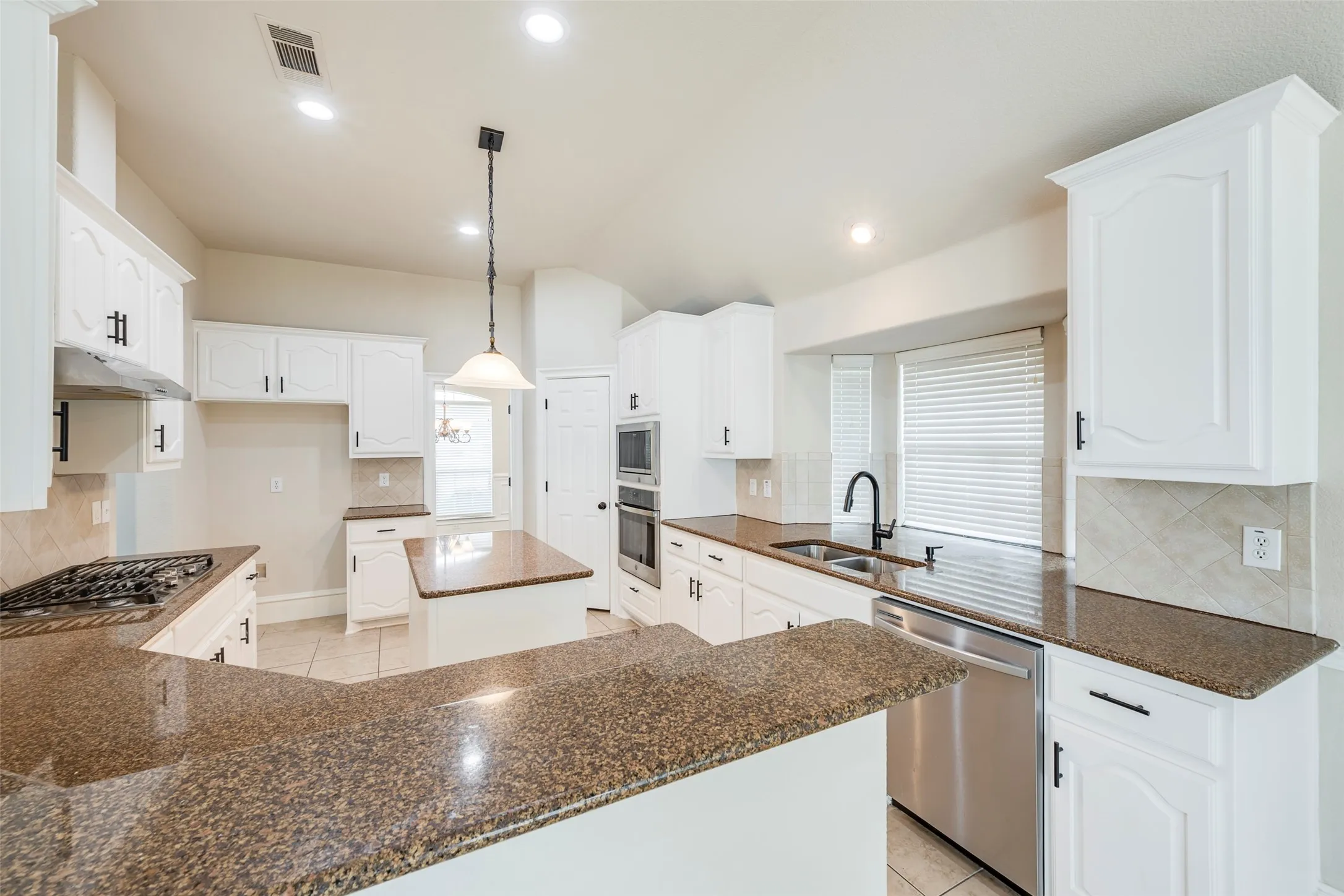Kitchen featuring white cabinetry, granite countertops, tile flooring, stainless steel appliances, and a central island