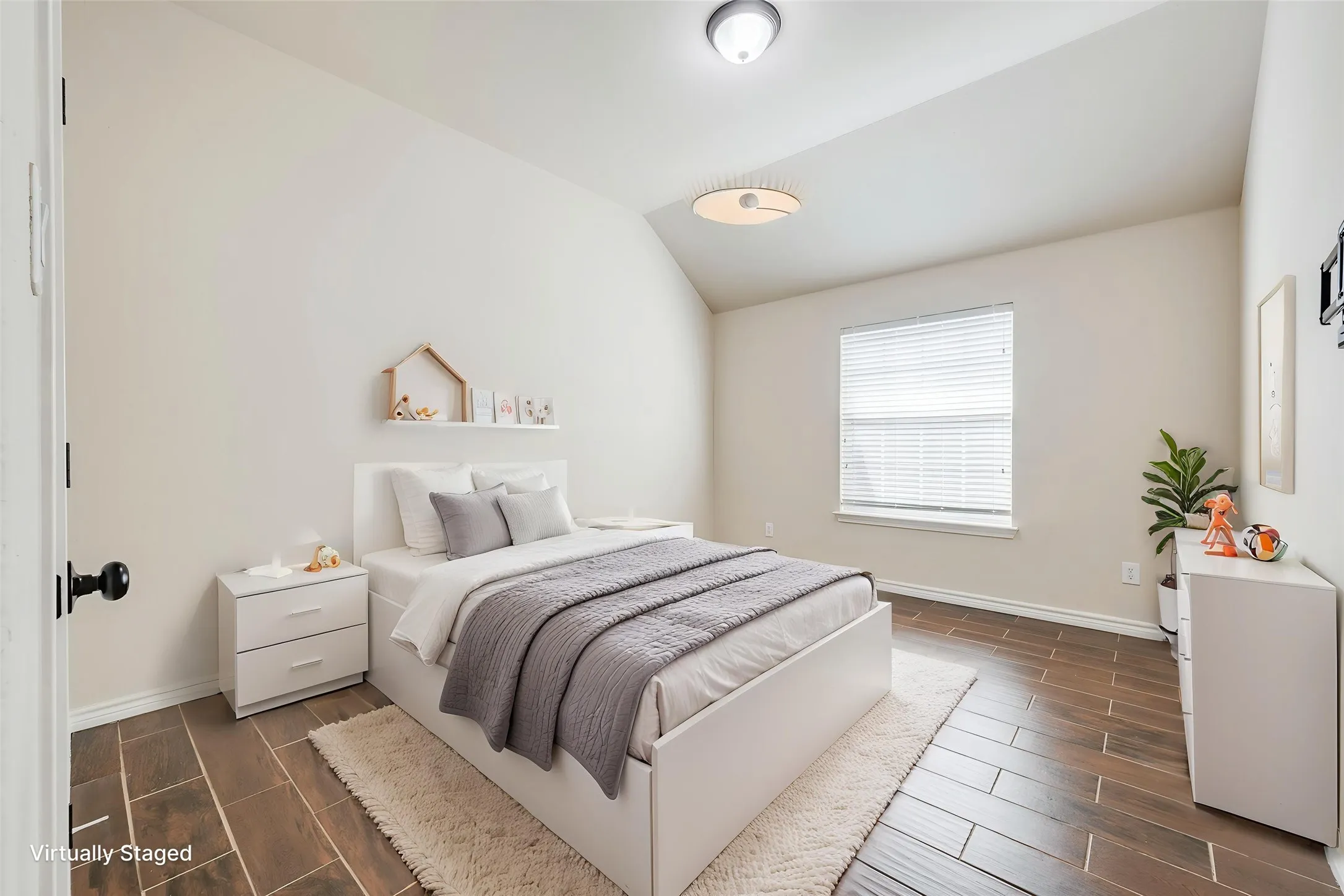 Wood-finish flooring, vaulted ceiling, white walls, single window with blinds, and a flush-mount ceiling light