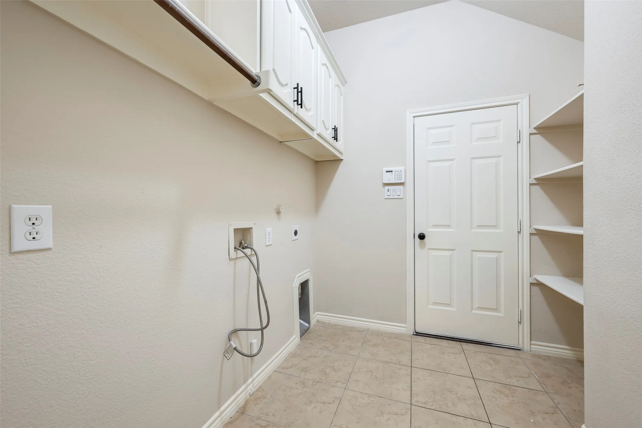 Vaulted ceiling with overhead cabinetry, built-in shelving, tile flooring, and a utility hookup area