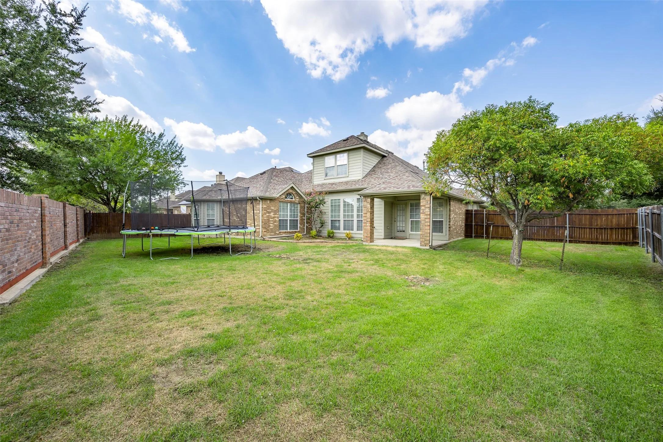 Expansive backyard featuring a red brick perimeter fence, wood panel fencing, and mature trees