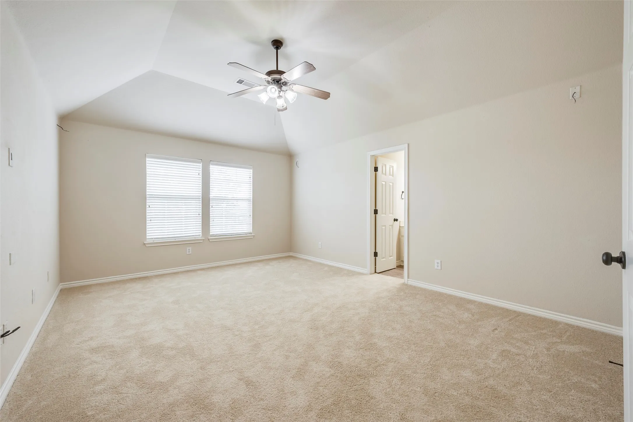 Vaulted ceiling with a ceiling fan, two windows with blinds, and neutral carpeting