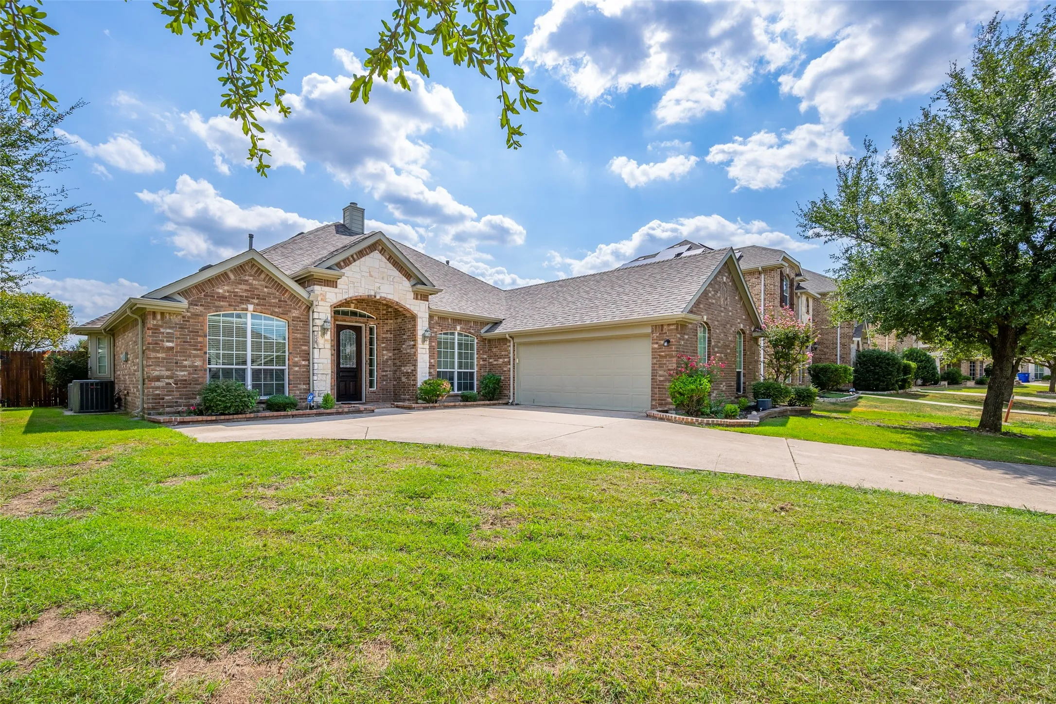 Brick and stone facade, arched entryway, bay windows, attached garage, and a concrete driveway