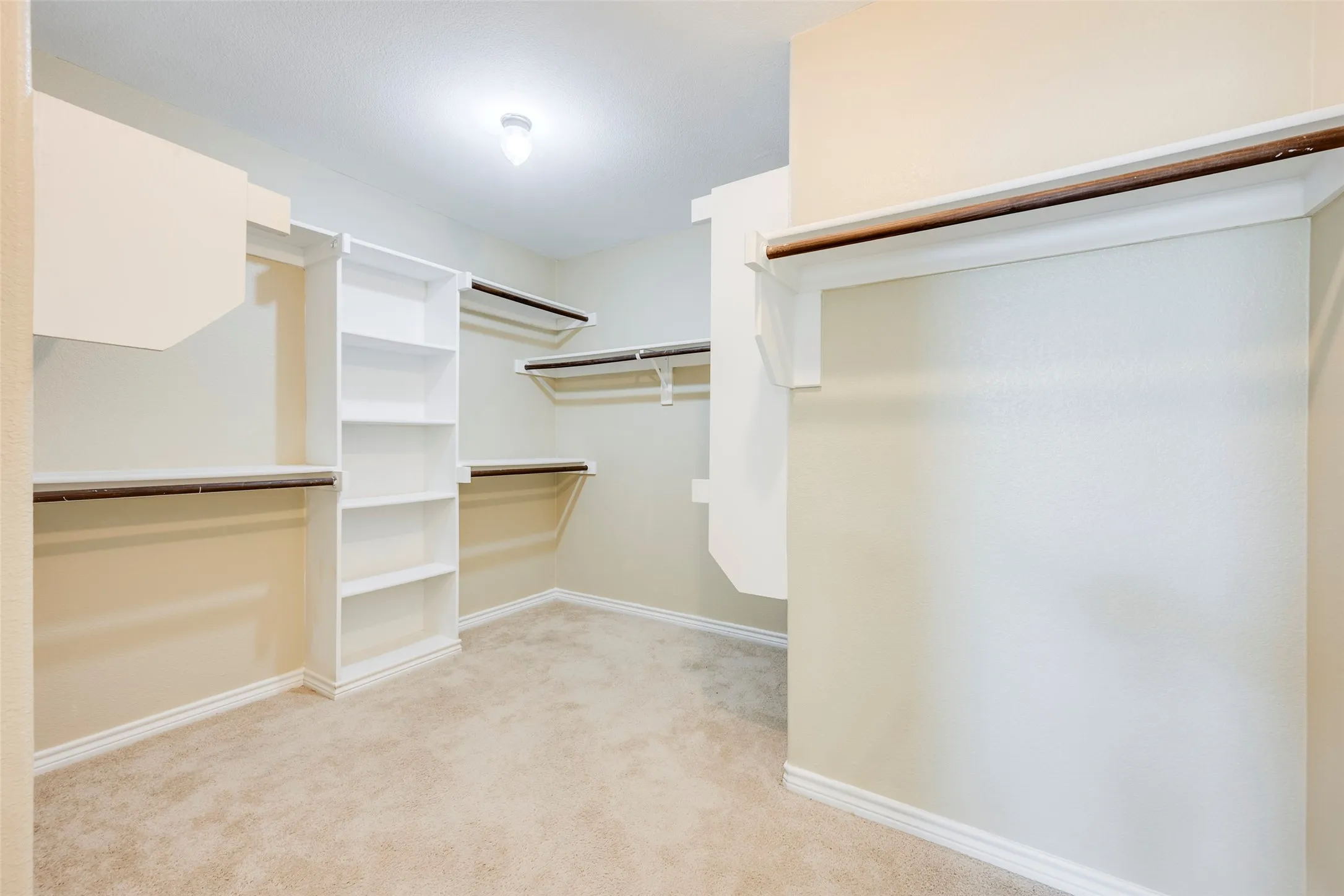 Recessed lighting, built-in shelving, multiple hanging rods, and neutral-toned carpeting