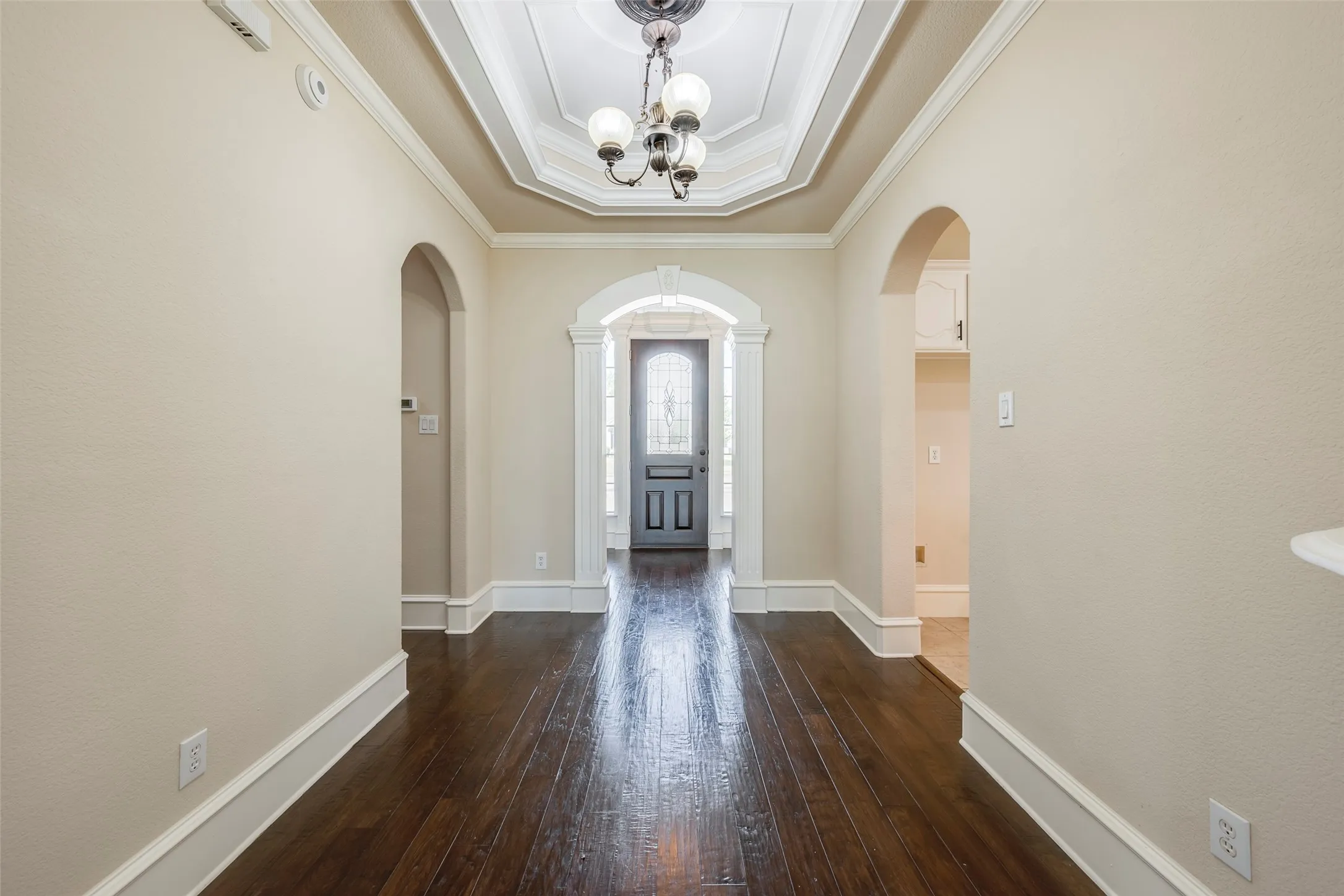 Foyer featuring wood-finish flooring, a tray ceiling, an ornate chandelier, and arched doorways