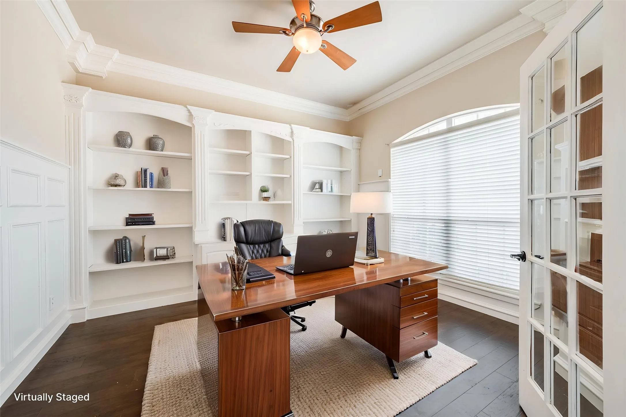 Built-in shelving, wood-finish flooring, paneled walls, crown molding, and an arched window