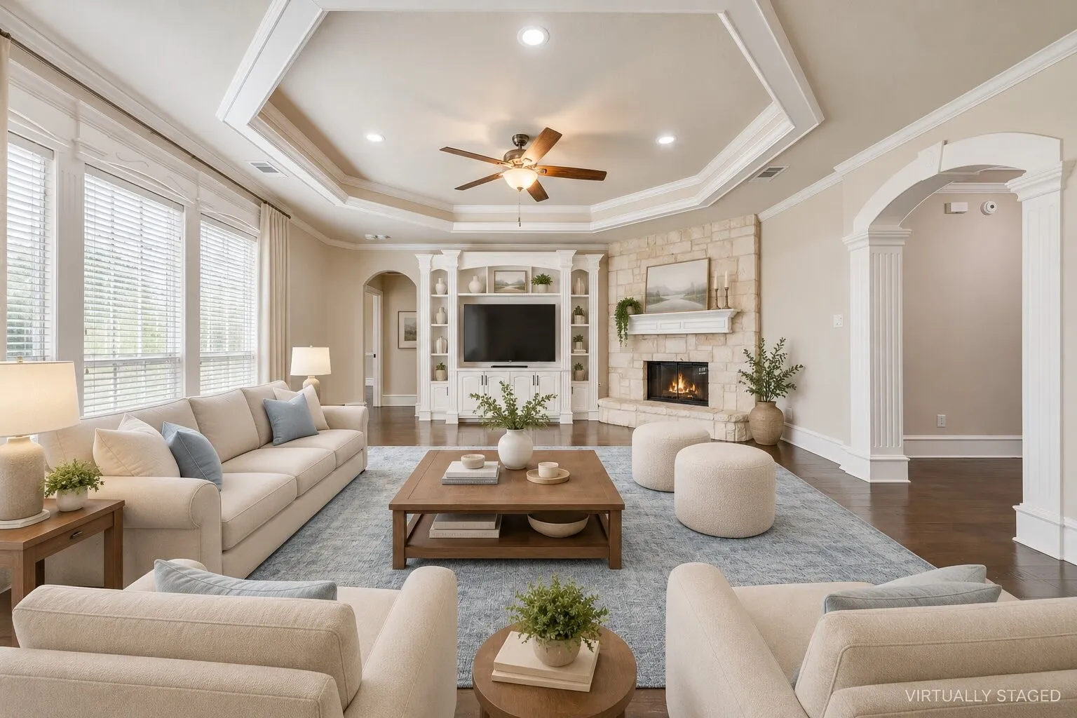 Tray ceiling with recessed lighting and a ceiling fan, stone-clad fireplace, built-in media cabinetry, dark wood-finish flooring, and arched doorways