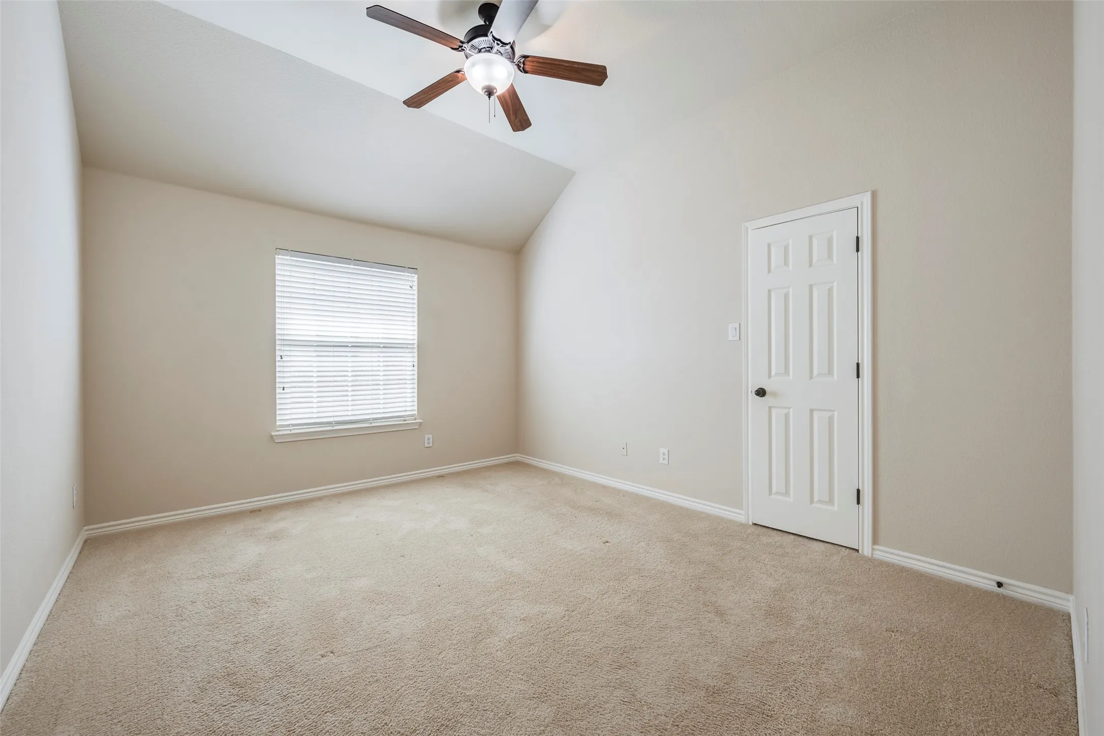 Vaulted ceiling with a ceiling fan, neutral wall paint, carpet flooring, and a paneled door with a black doorknob