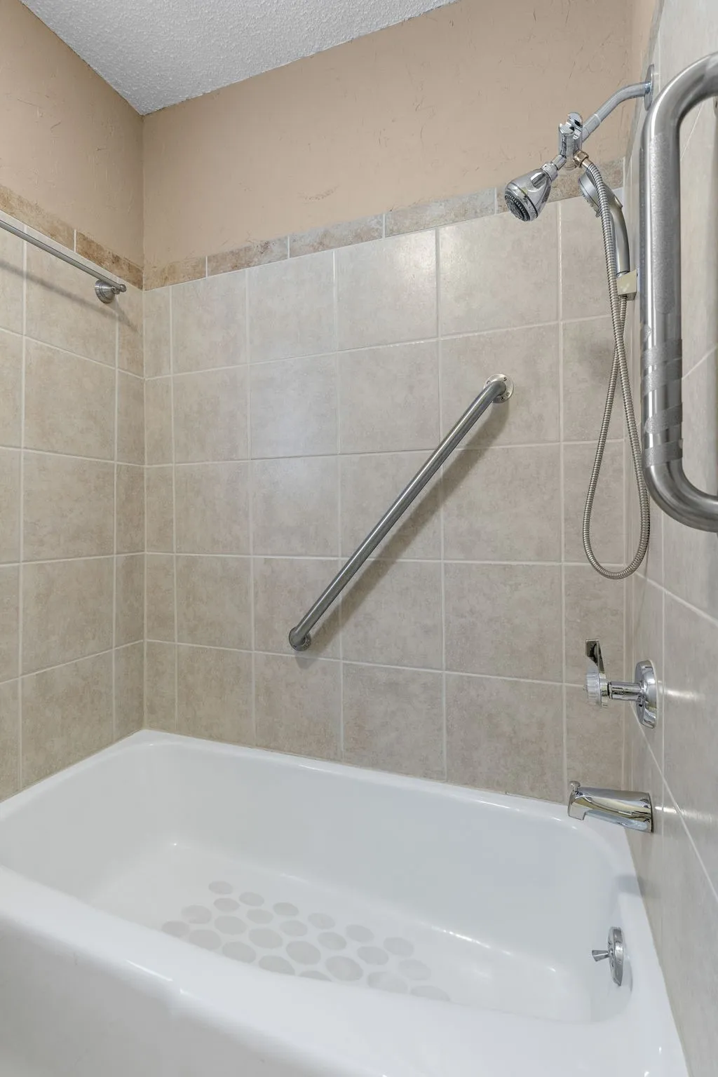 Tub/shower combination featuring light-toned tile surround, chrome fixtures, and integrated grab bars