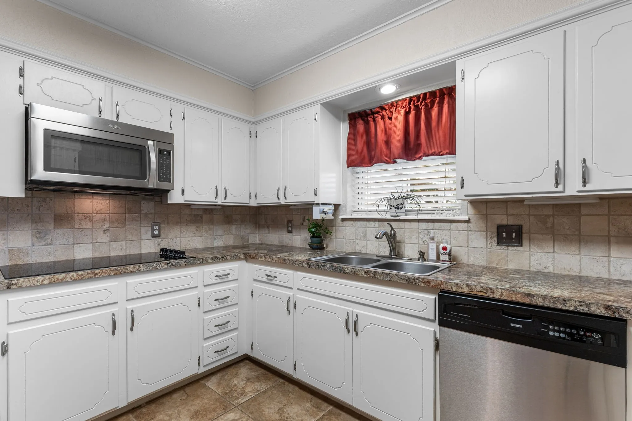 Stainless steel microwave, integrated dishwasher, dual basin sink, tile backsplash, and patterned countertops