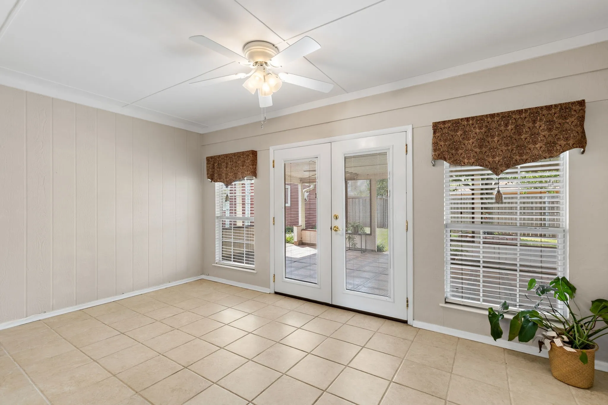 Tile flooring, white French doors, ceiling fan with integrated lighting, two windows with blinds, and paneled wall accents