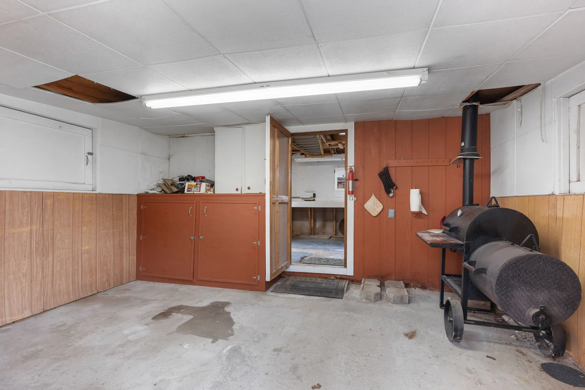 Utility room with concrete flooring, drop ceiling, and built-in cabinetry and built in smoker to be conveyed with the property.
