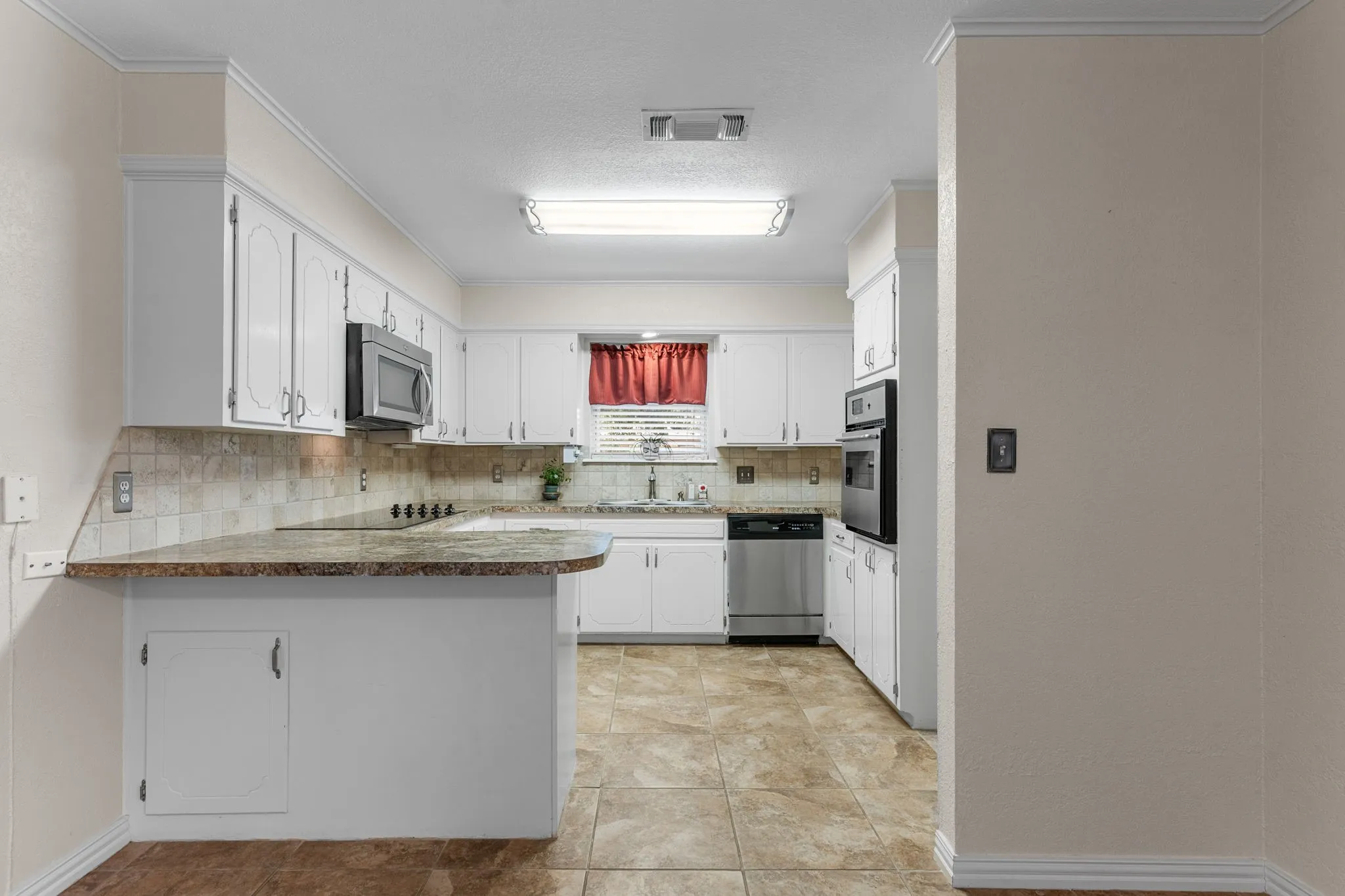 Kitchen featuring white cabinetry, stainless steel appliances, tile flooring, stone countertops, and a tile backsplash