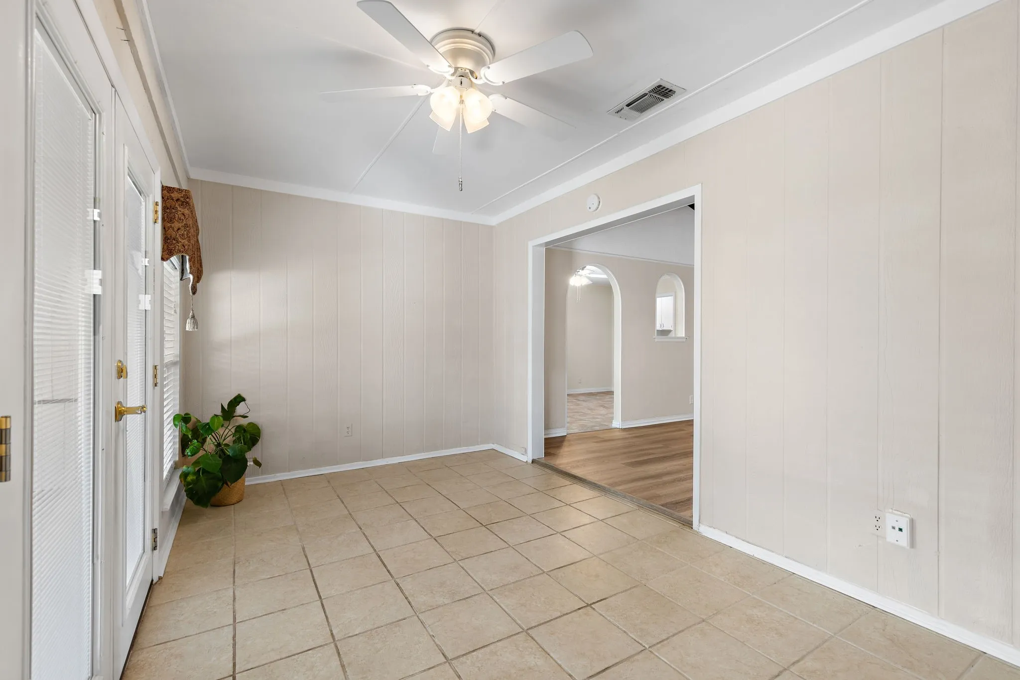 Tiled flooring, paneled wall finishes, ceiling fan, and double exterior doors with integrated blinds