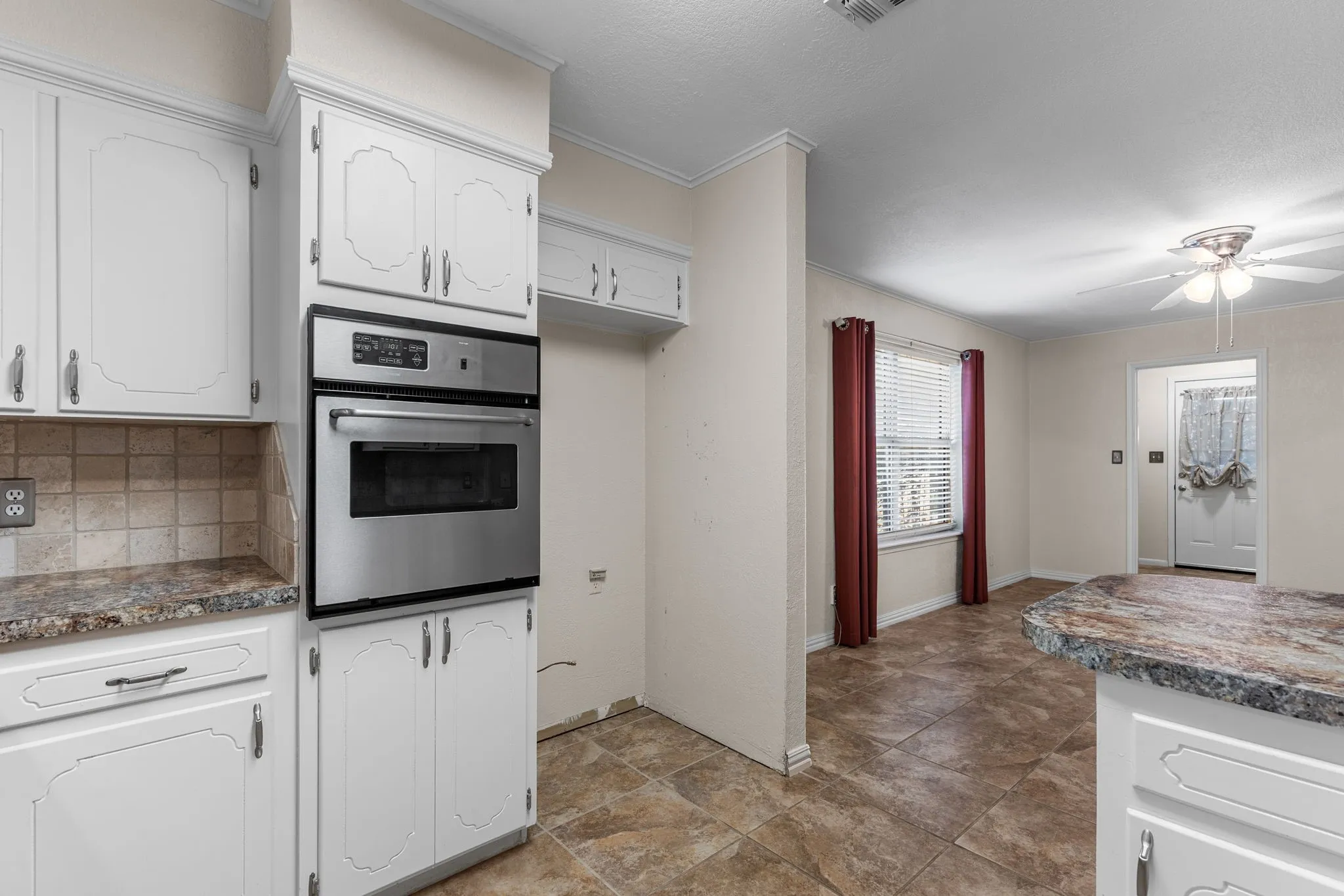 White cabinetry with decorative fronts, stainless steel built-in oven, tile backsplash, laminate countertops, and tile flooring