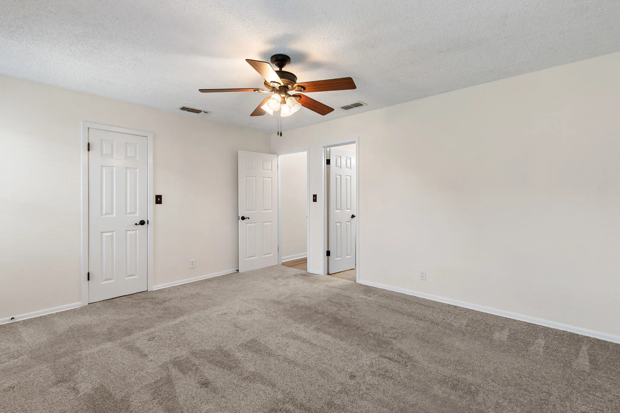 Primary with walk in closet and ensuite. Carpet flooring, ceiling fan with integrated lighting, and multiple paneled doors.