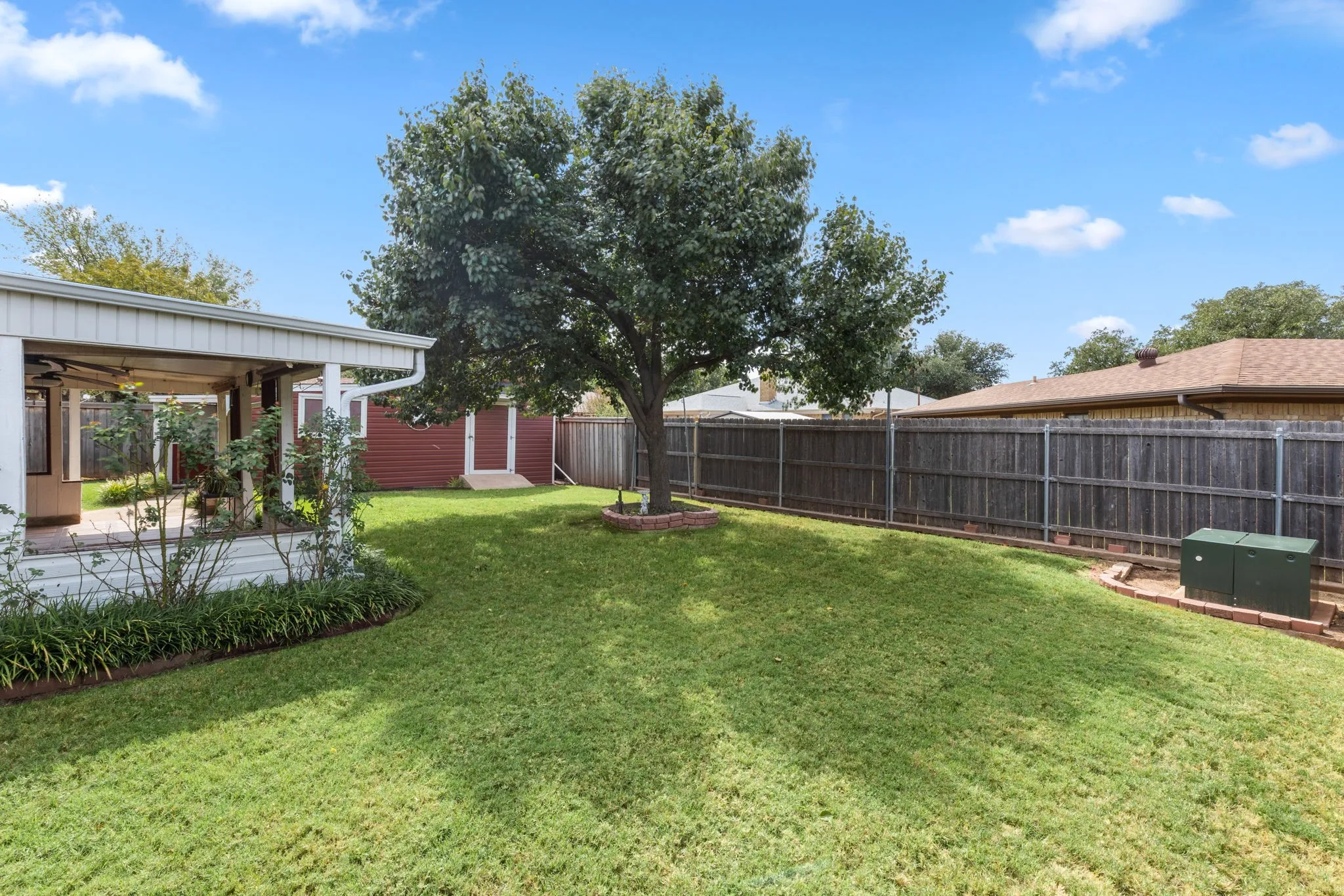 Expansive lawn area with a mature shade tree and a full privacy fence