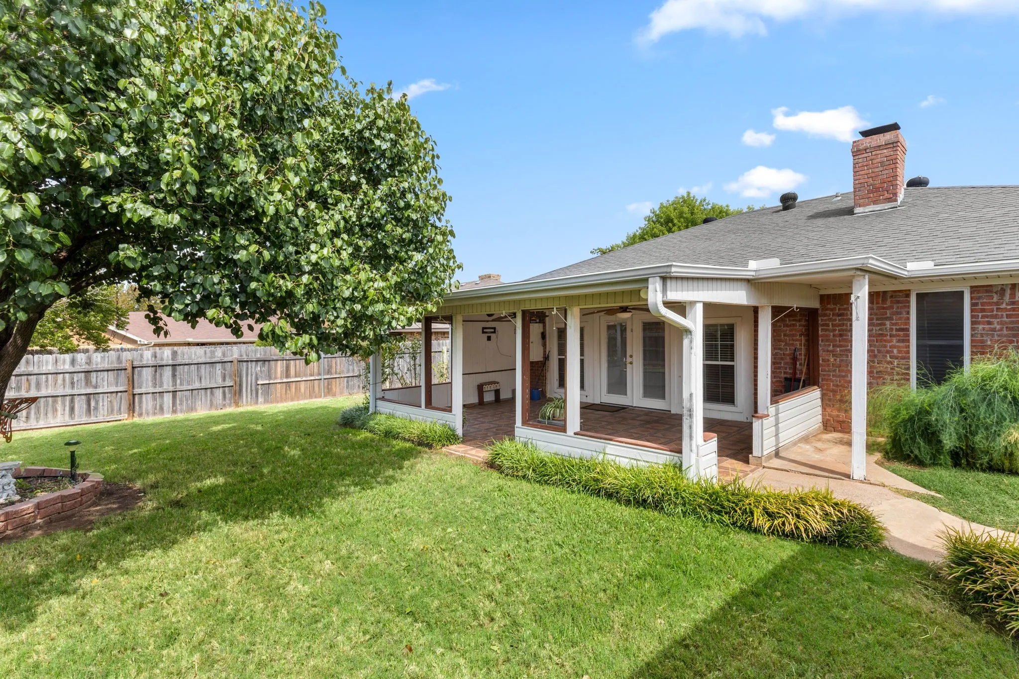 Expansive backyard featuring a mature tree, privacy fencing, and a covered brick patio with white French doors