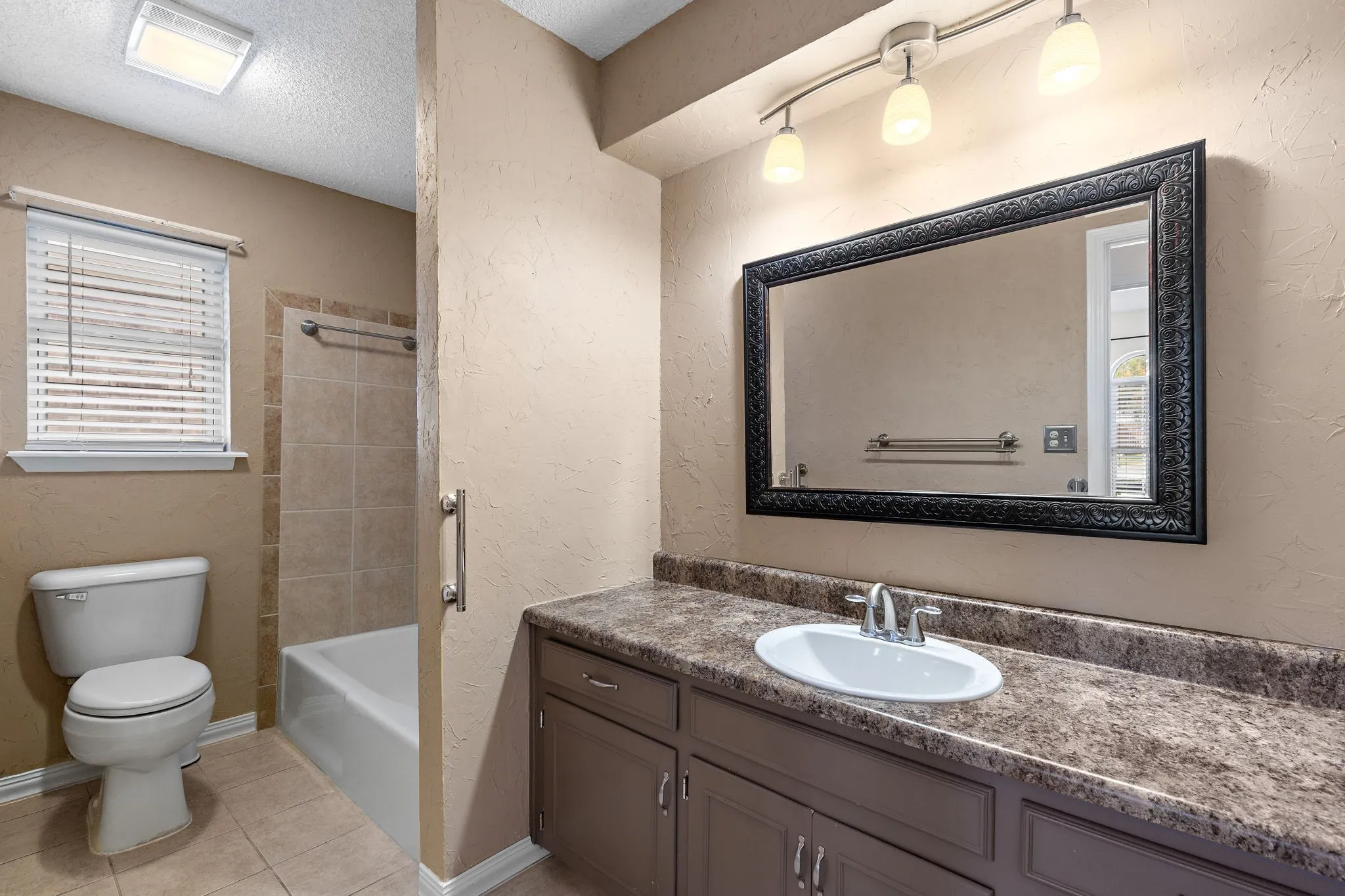 Second Bath - Vanity with an integrated sink, framed mirror, and track lighting and window for extra light.