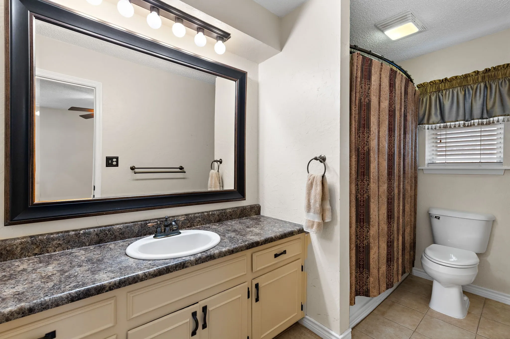 Primary Bath - Vanity with an integrated sink, dark-toned countertop, light cabinetry and window.