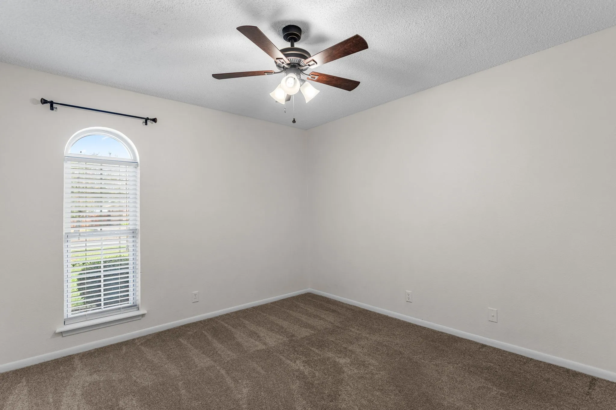 Bright corner bedroom with arched transom window featuring wood faux blinds, ceiling fan with integrated lighting, and new paint.