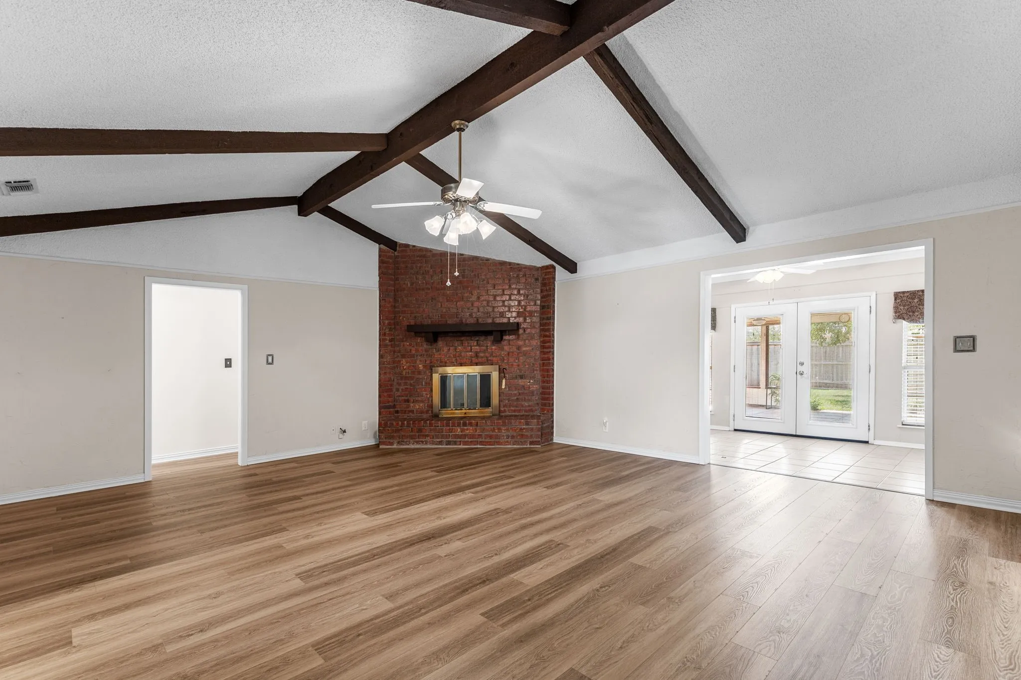 Vaulted ceiling with exposed wood beams, wood-finish flooring, brick-faced fireplace, and French doors to exterior