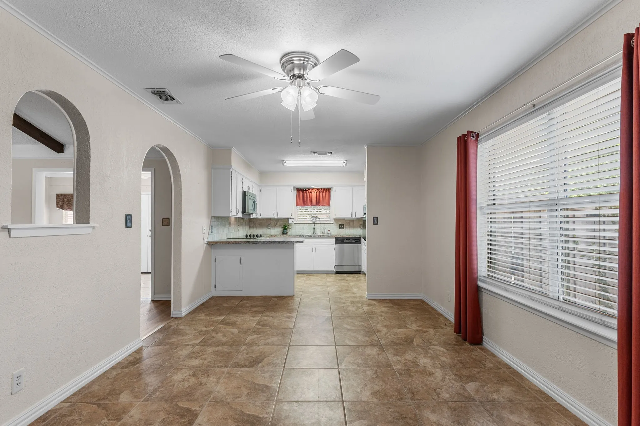 Arched doorways, tile flooring, window with blinds, ceiling fan, and white cabinetry