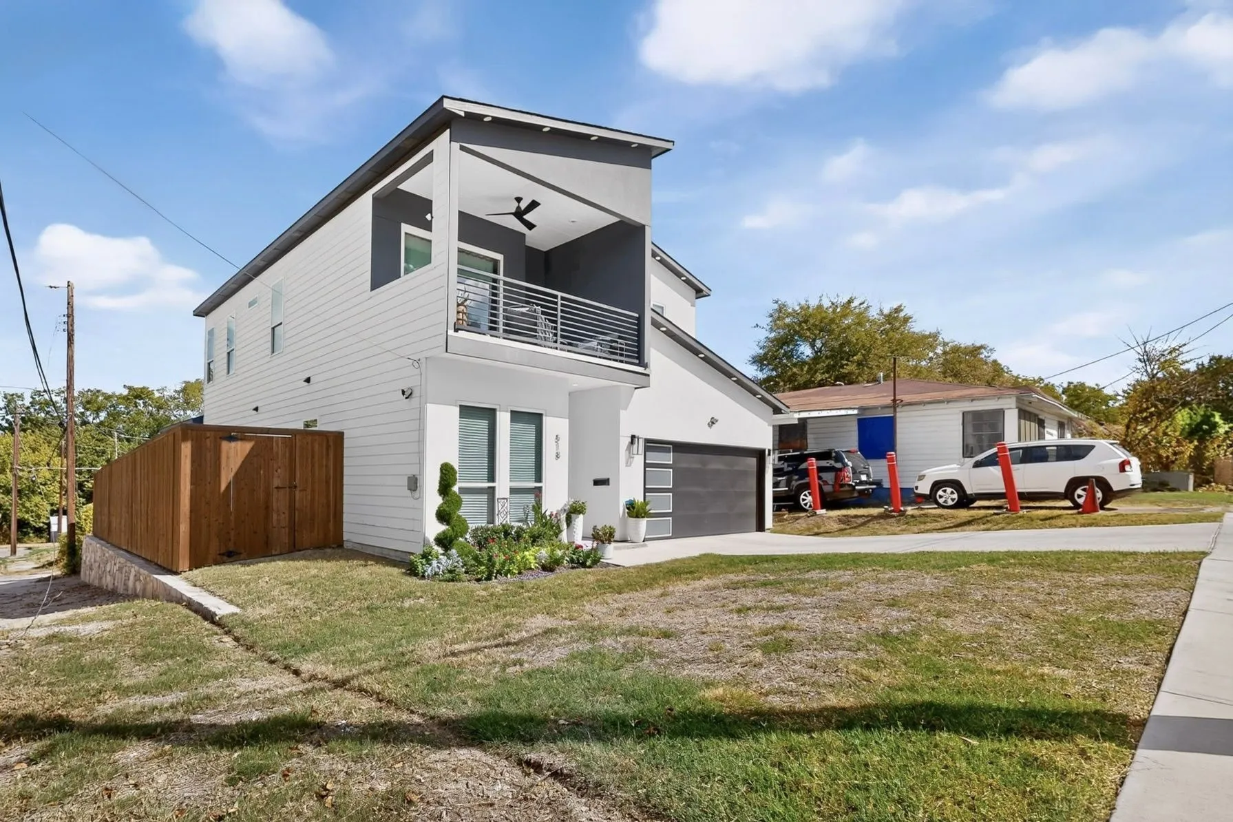 Contemporary exterior with white siding and dark trim, featuring a second-story balcony with a ceiling fan, a modern garage door, and a privacy fence