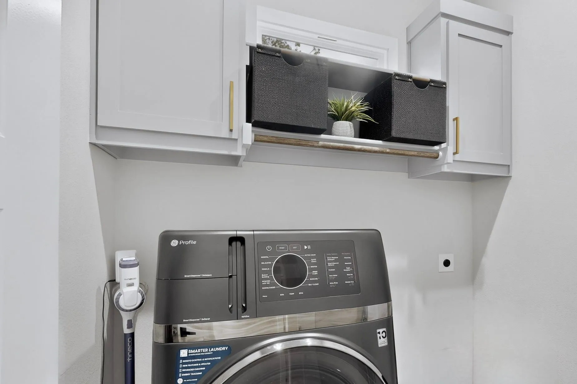 White wall-mounted cabinetry with gold-tone hardware, open shelving with a wooden rod, and a window providing natural light