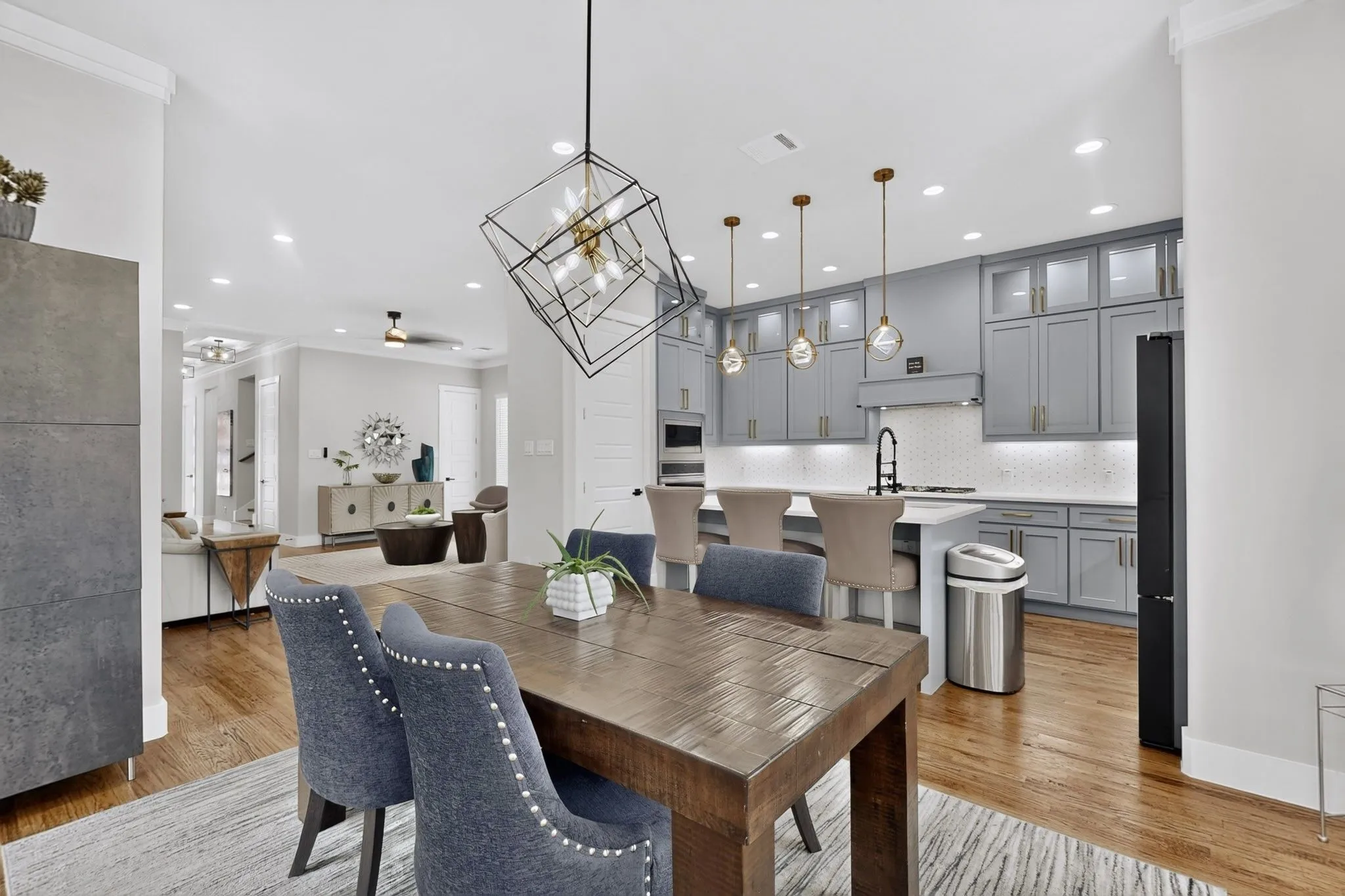 Wood-finish flooring throughout, modern kitchen with gray cabinetry, kitchen island with seating, geometric lighting fixture, and recessed lighting