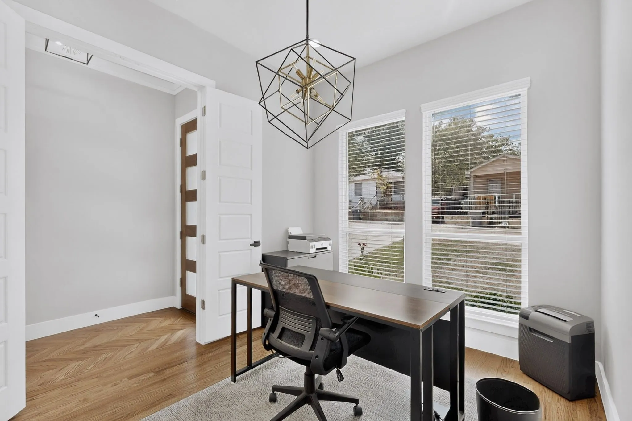 Herringbone wood-finish flooring, two window openings, recessed lighting, and a modern geometric pendant light fixture