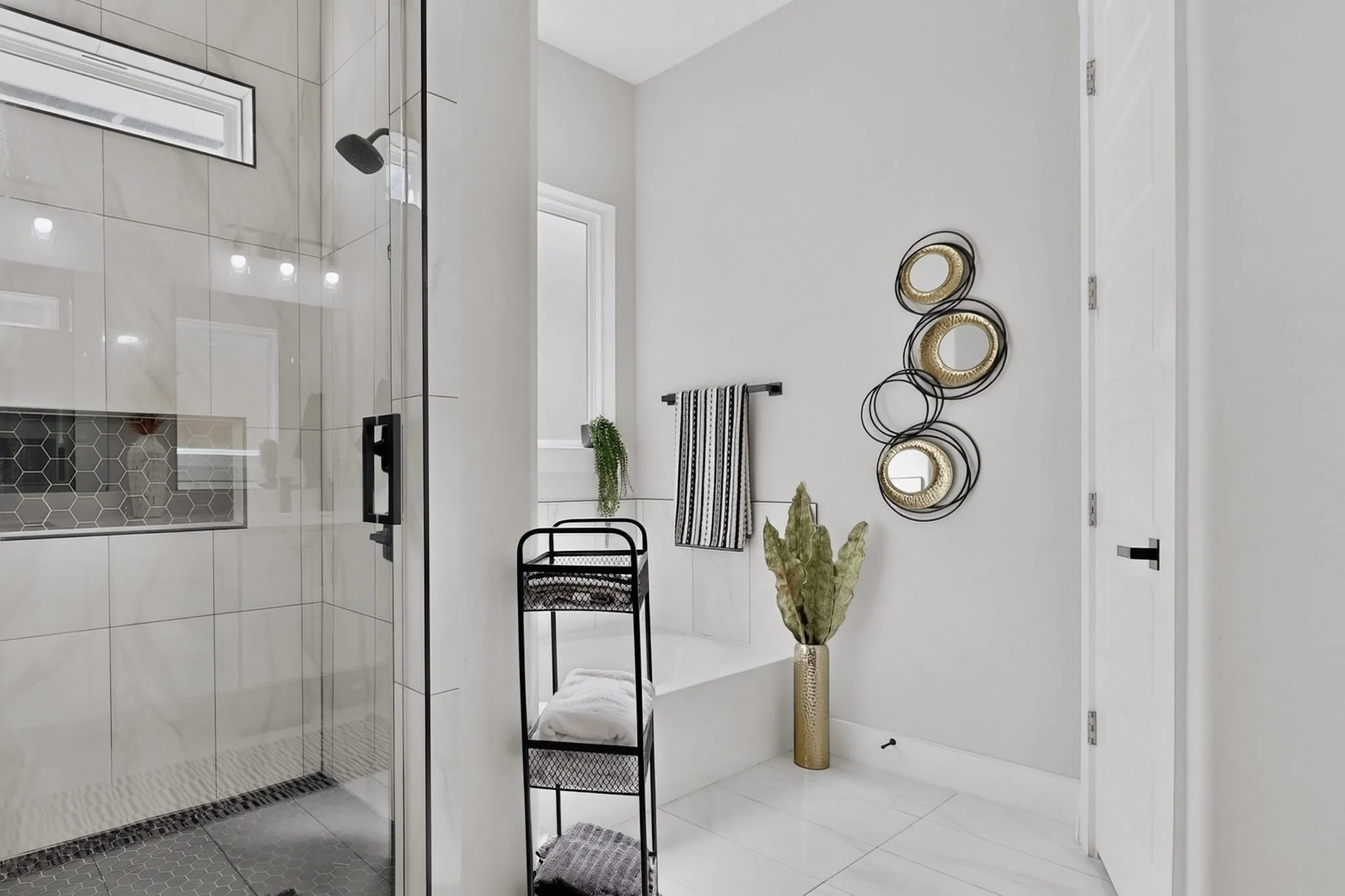 Glass-enclosed shower with a matte black shower head, built-in tiled niche, and dark pebble floor