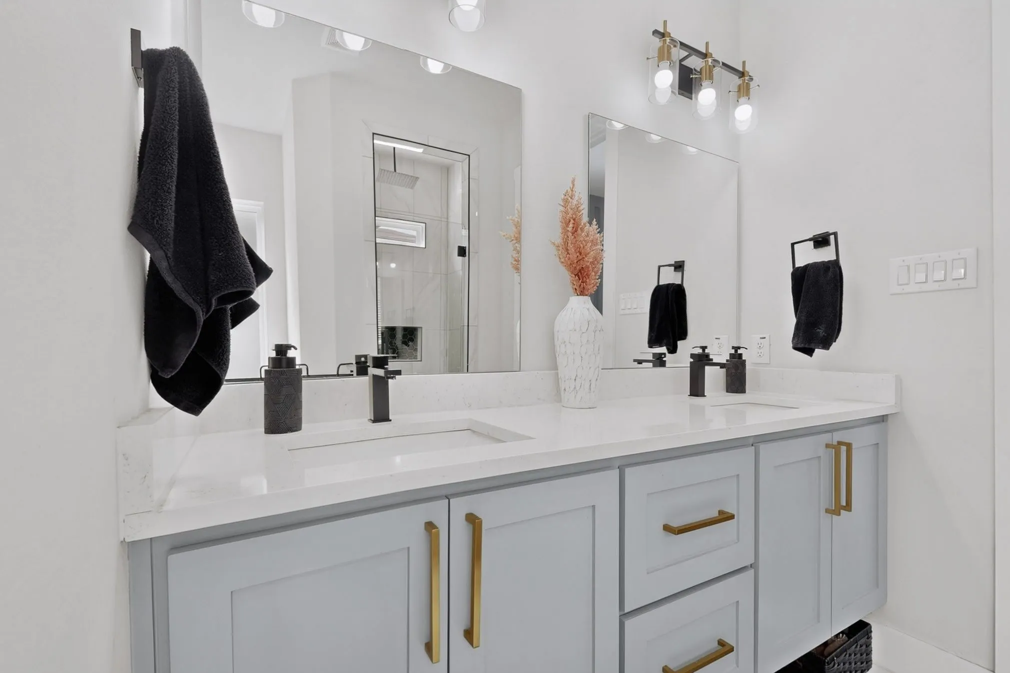 Dual vanity with light gray cabinetry, gold-tone hardware, and white countertops
