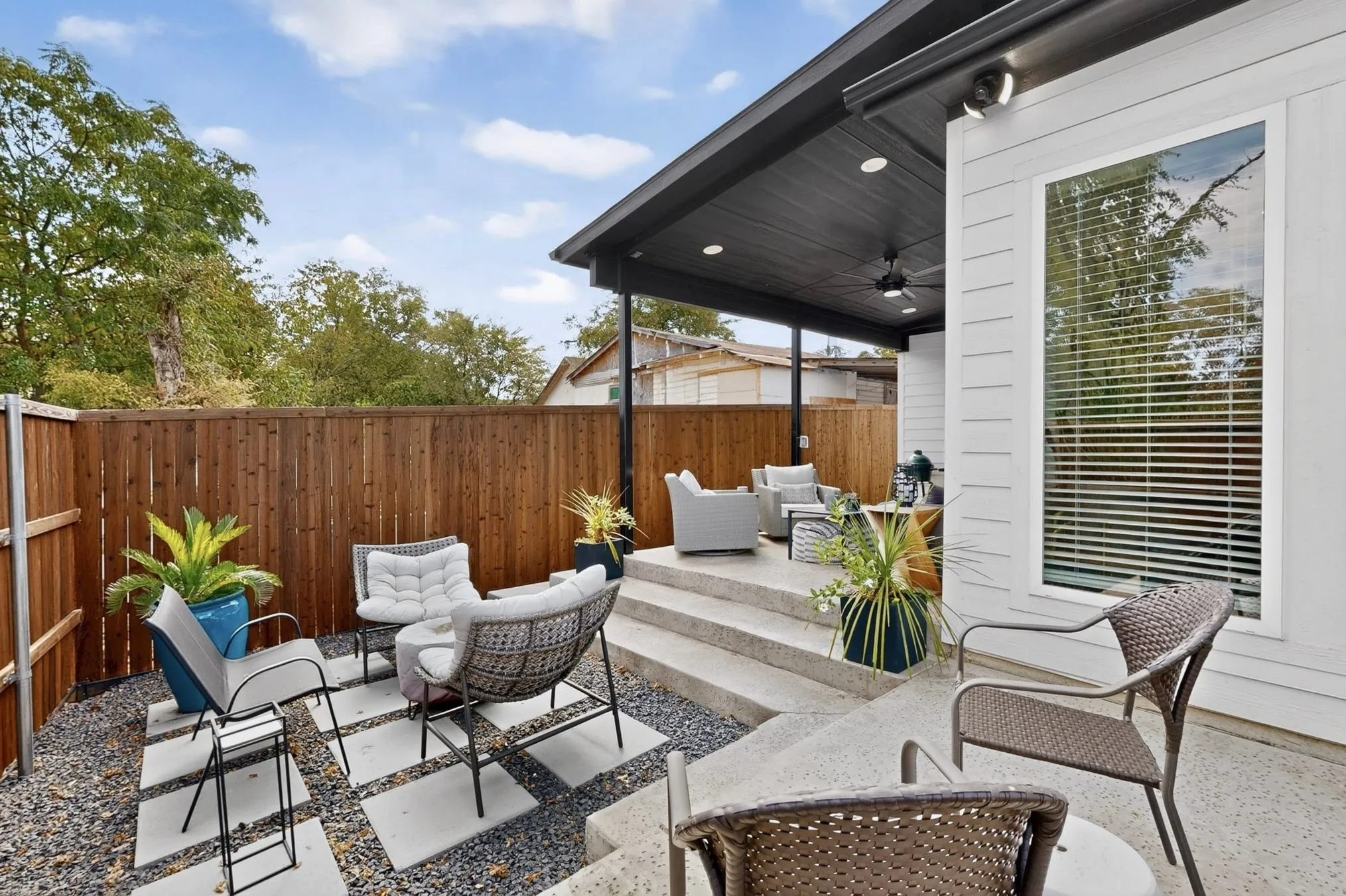 Private outdoor patio space featuring a wood fence, concrete steps, and a covered area with a ceiling fan