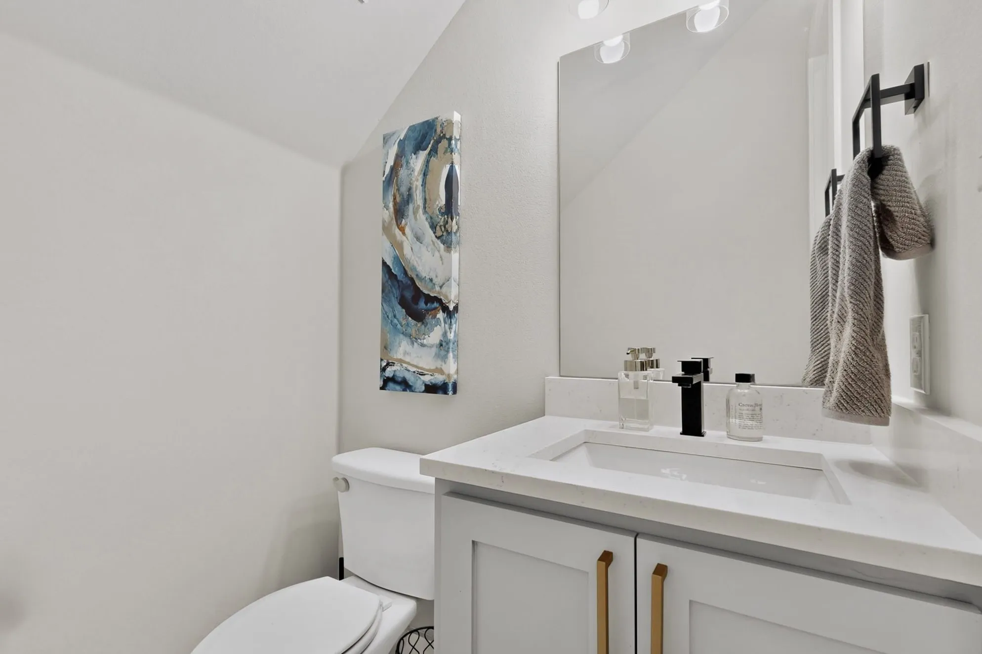 Vanity with white countertop, integrated rectangular sink, matte black faucet, and light gray cabinetry with gold-toned hardware