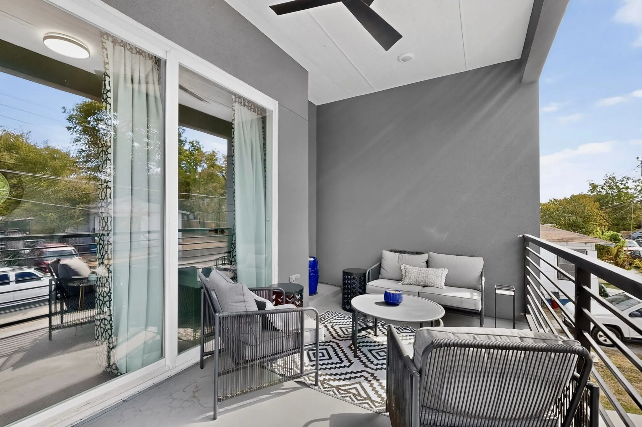 Outdoor balcony featuring a ceiling fan, sliding glass doors, white trim, and a black metal railing
