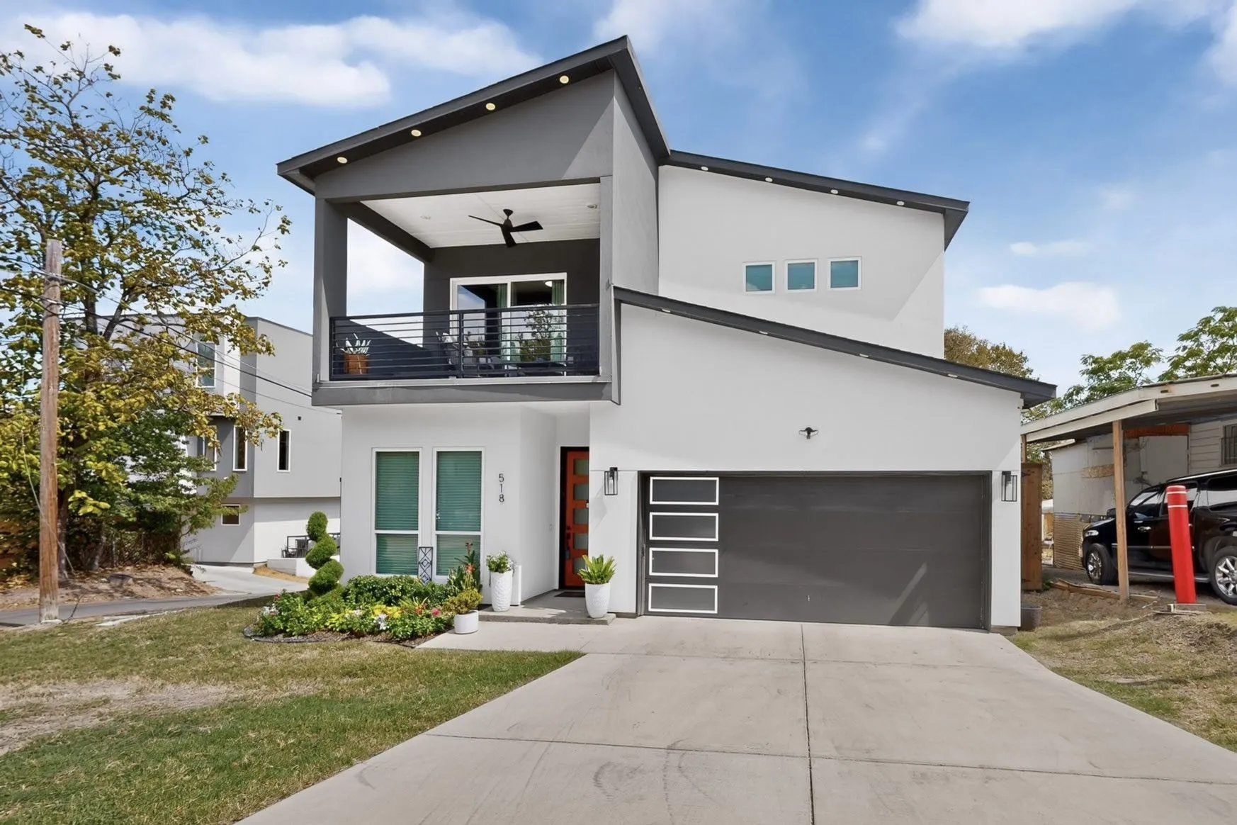 Contemporary facade with a covered second-story balcony featuring a ceiling fan, a modern garage door with frosted glass panels, an accent-colored entry door, and a concrete driveway