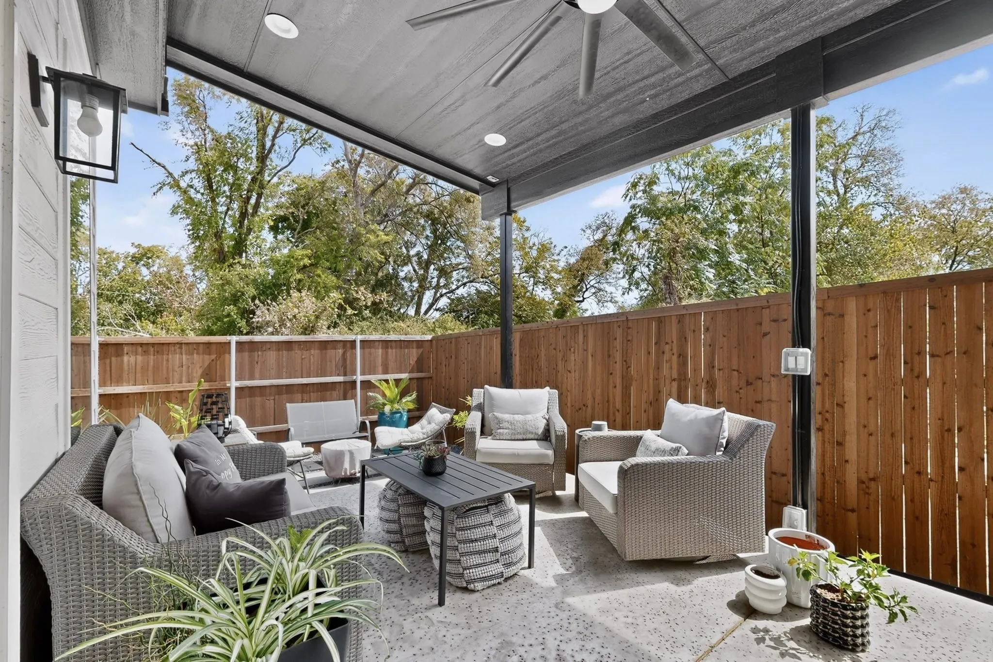 Covered patio with concrete flooring, wood privacy fencing, and an exterior wall lantern