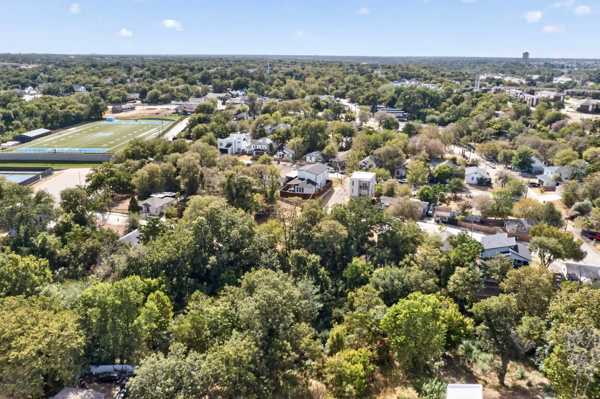 Aerial perspective showcasing a residential area with extensive tree coverage and a distant athletic field