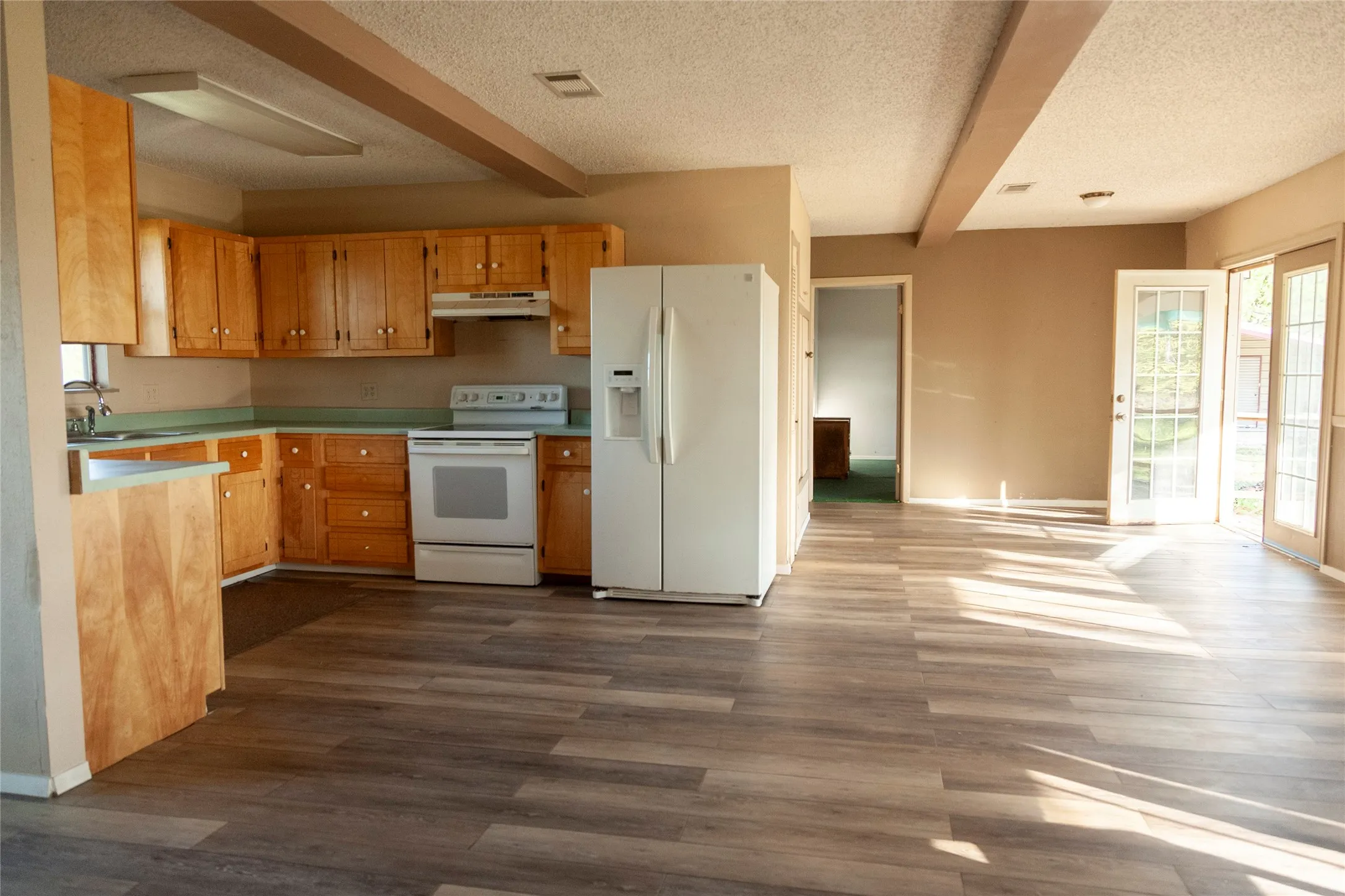 Open-concept kitchen and living area featuring wood-finish flooring, light wood cabinetry, white kitchen appliances, and glass-paned double doors