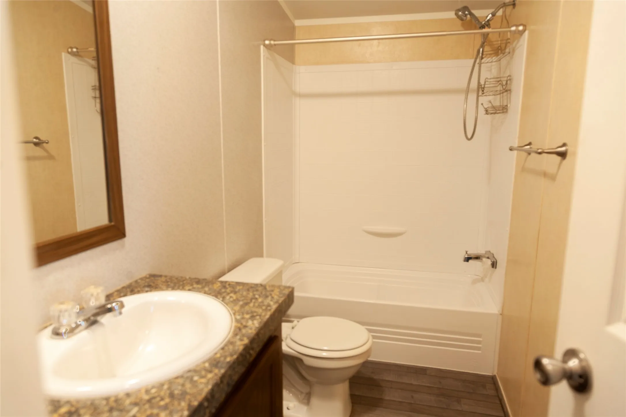 Bathroom featuring a white tub/shower combination, a vanity with an integrated sink and stone-look countertop, a wooden-framed mirror, and wood-finish flooring