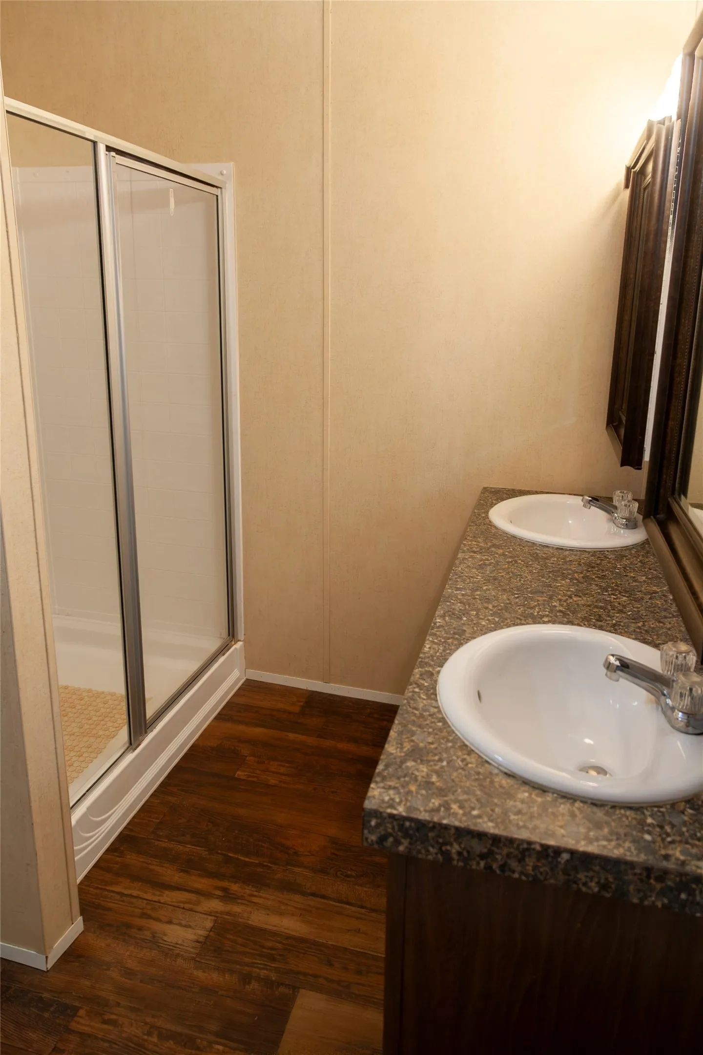 Dual basin vanity with a stone-finish countertop, wood-finish flooring, and a glass-enclosed shower